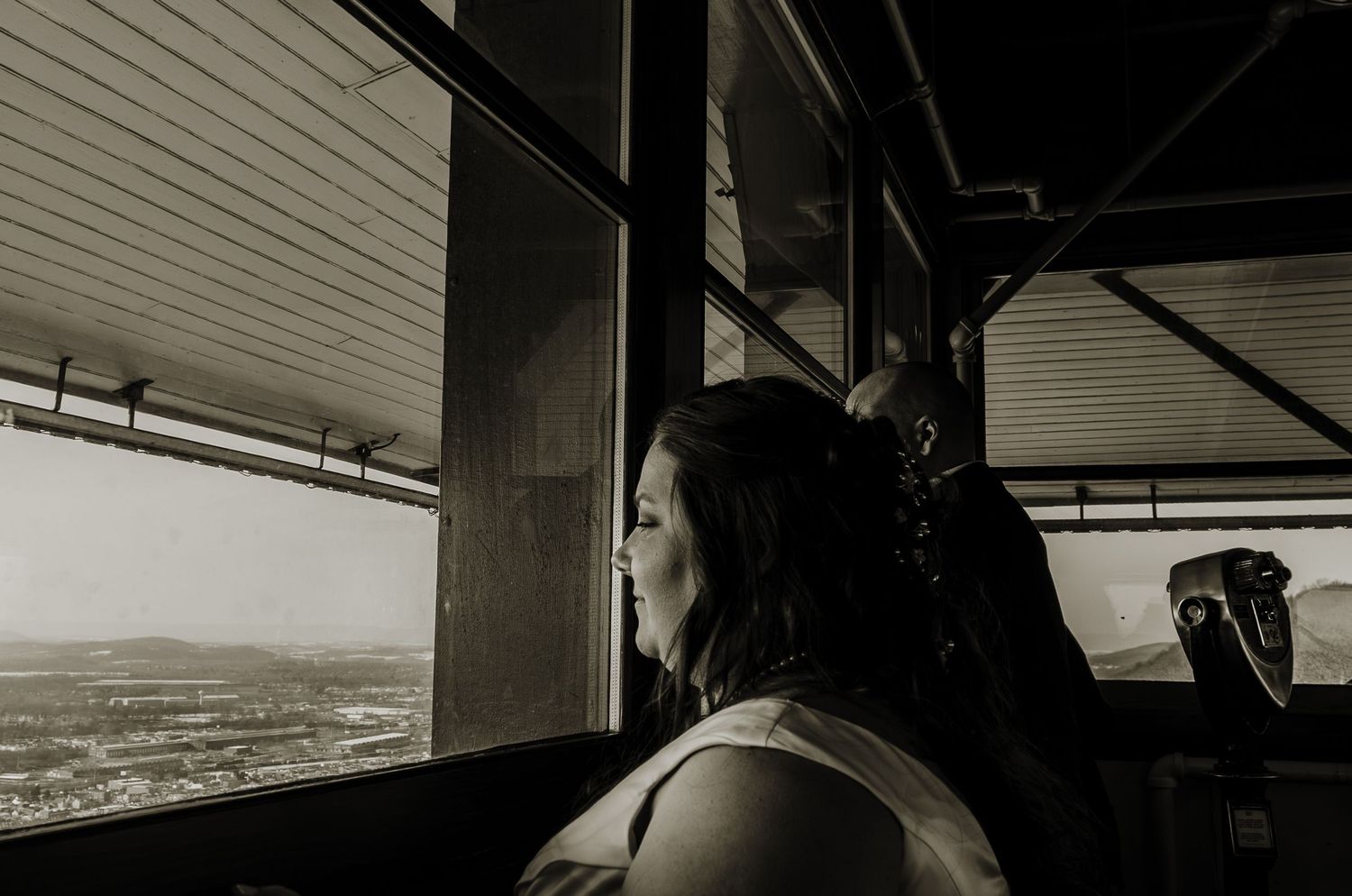 Black and white photo of a woman gazing out large windows from an elevated observation deck.