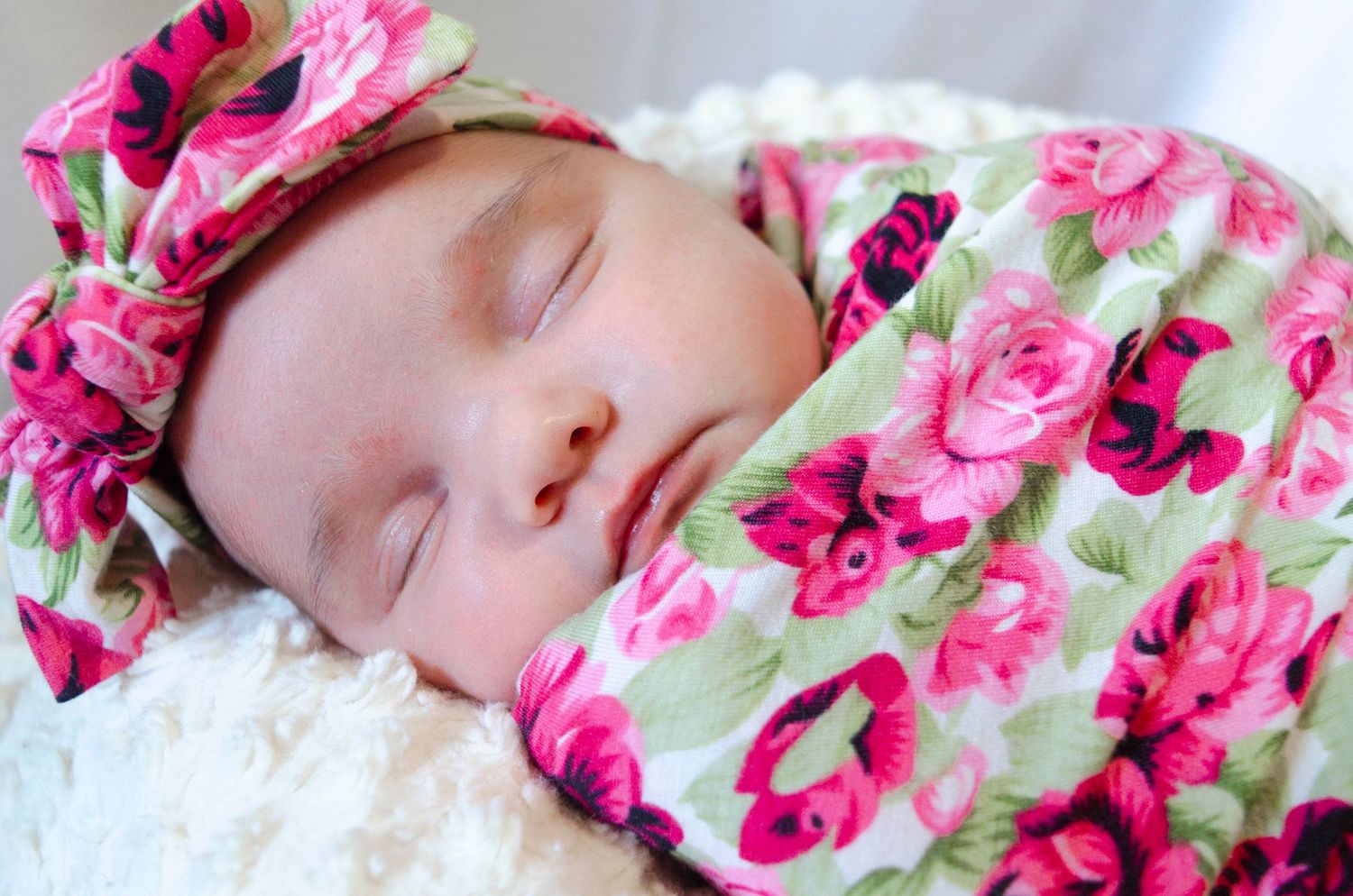 Sleeping newborn baby girl wrapped in a pink floral swaddle blanket with matching bow headband.