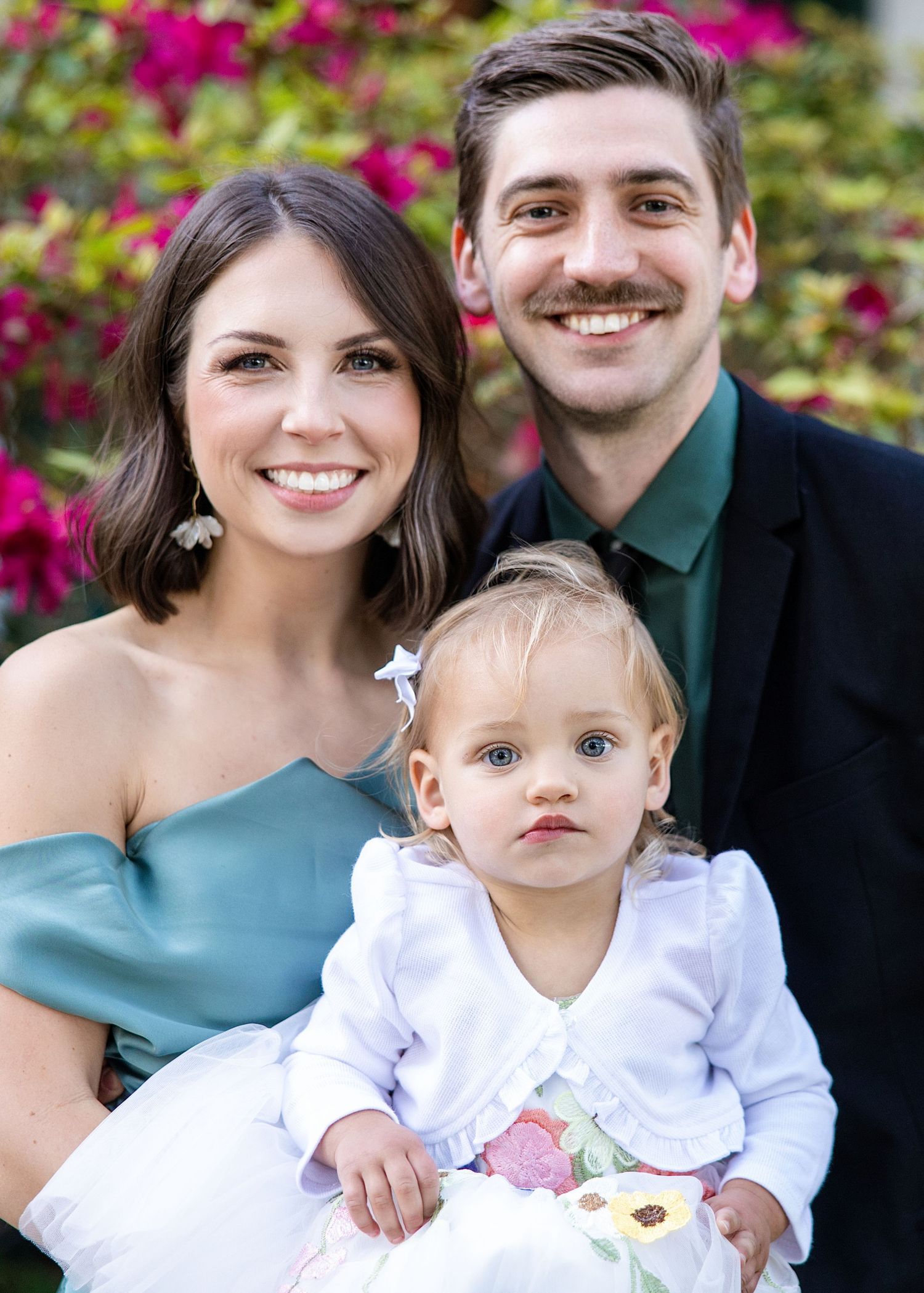 family of 3 holding each other in front of a bush blooming with purple flowers