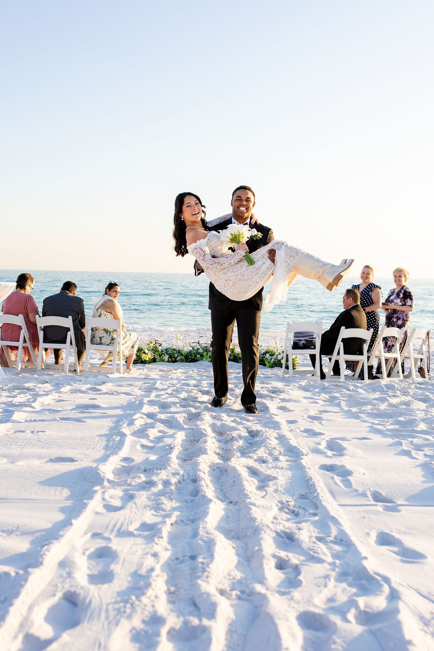 husband carrying his new bride down the aisle of their own beach wedding