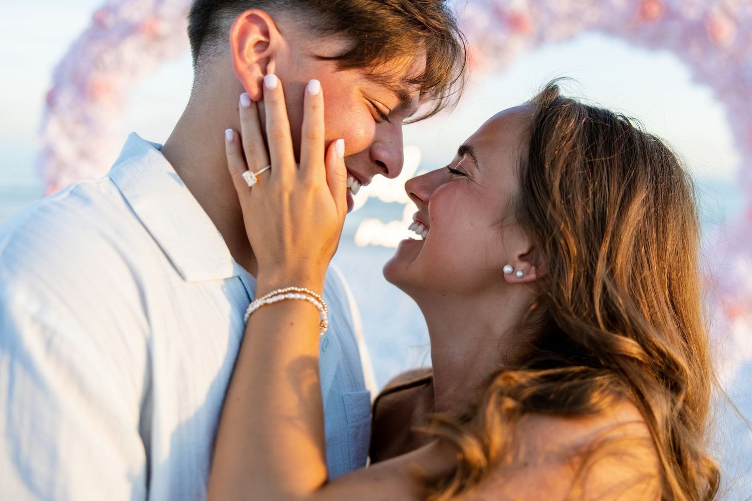 Happy newly engaged couple sharing a romantic moment on beach with woman displaying her ring.