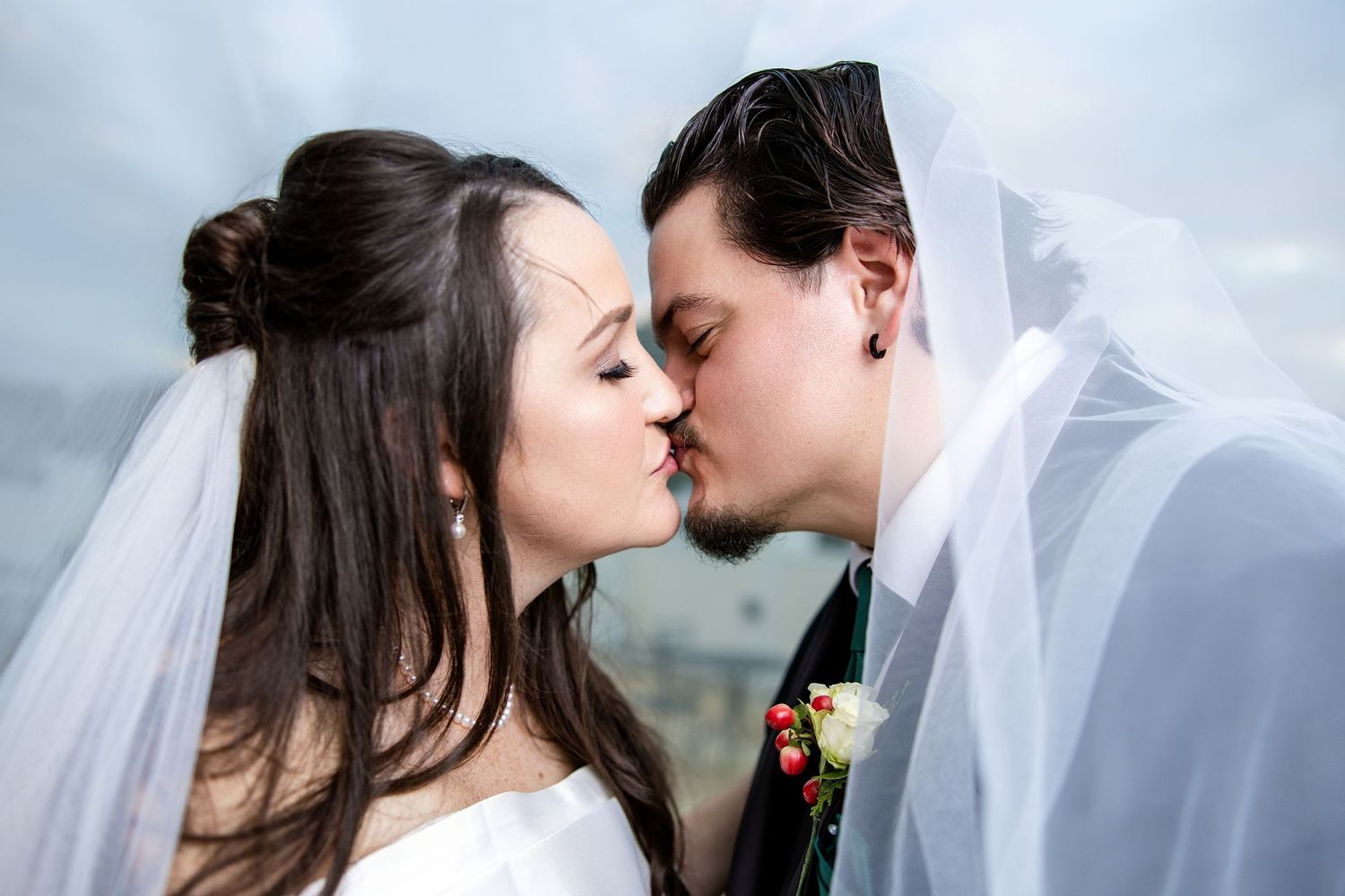 Bride and groom sharing a romantic kiss under a white veil on their wedding day.