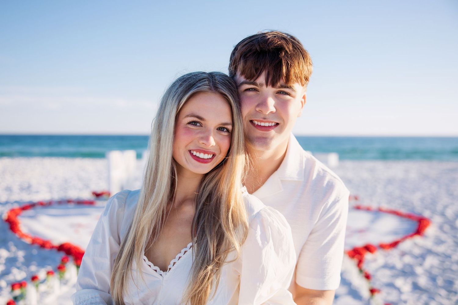 Happy couple posing on a romantic beach setup with red rose petals heart decoration on a sunny day.
