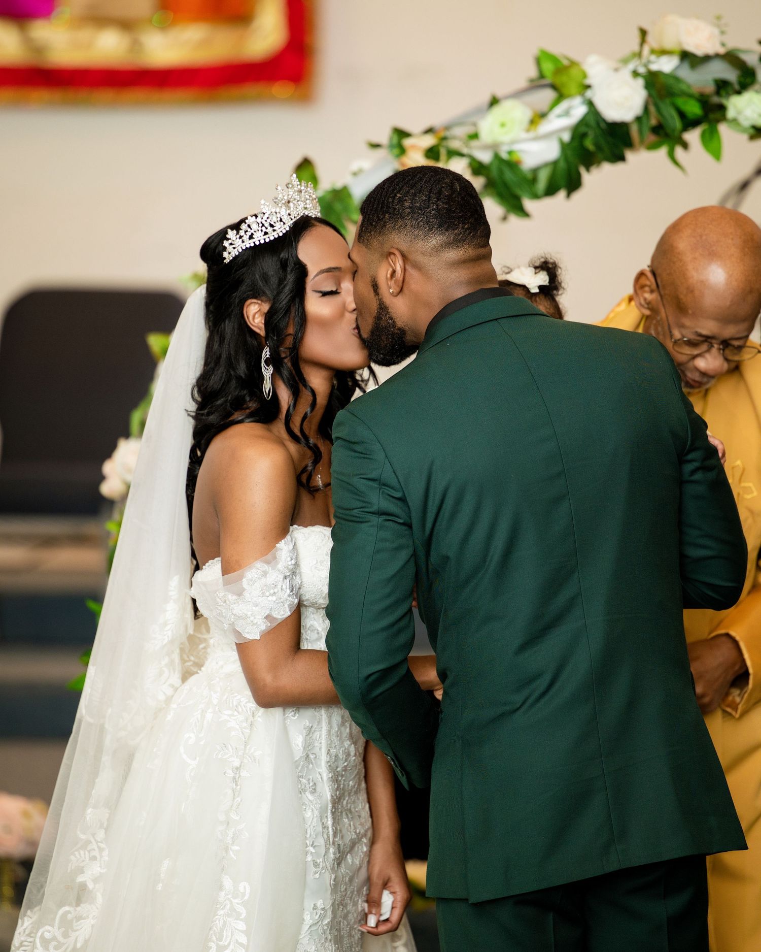 Bride and groom share first kiss at altar during elegant church wedding ceremony, bride wearing tiara and white gown.
