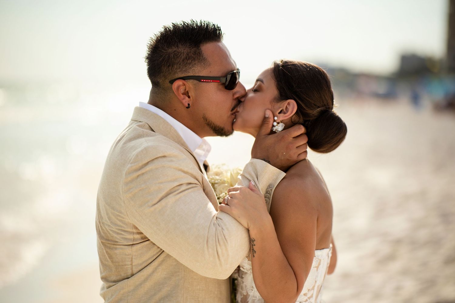 Bride and groom share a romantic kiss on the beach during their wedding ceremony at sunset.