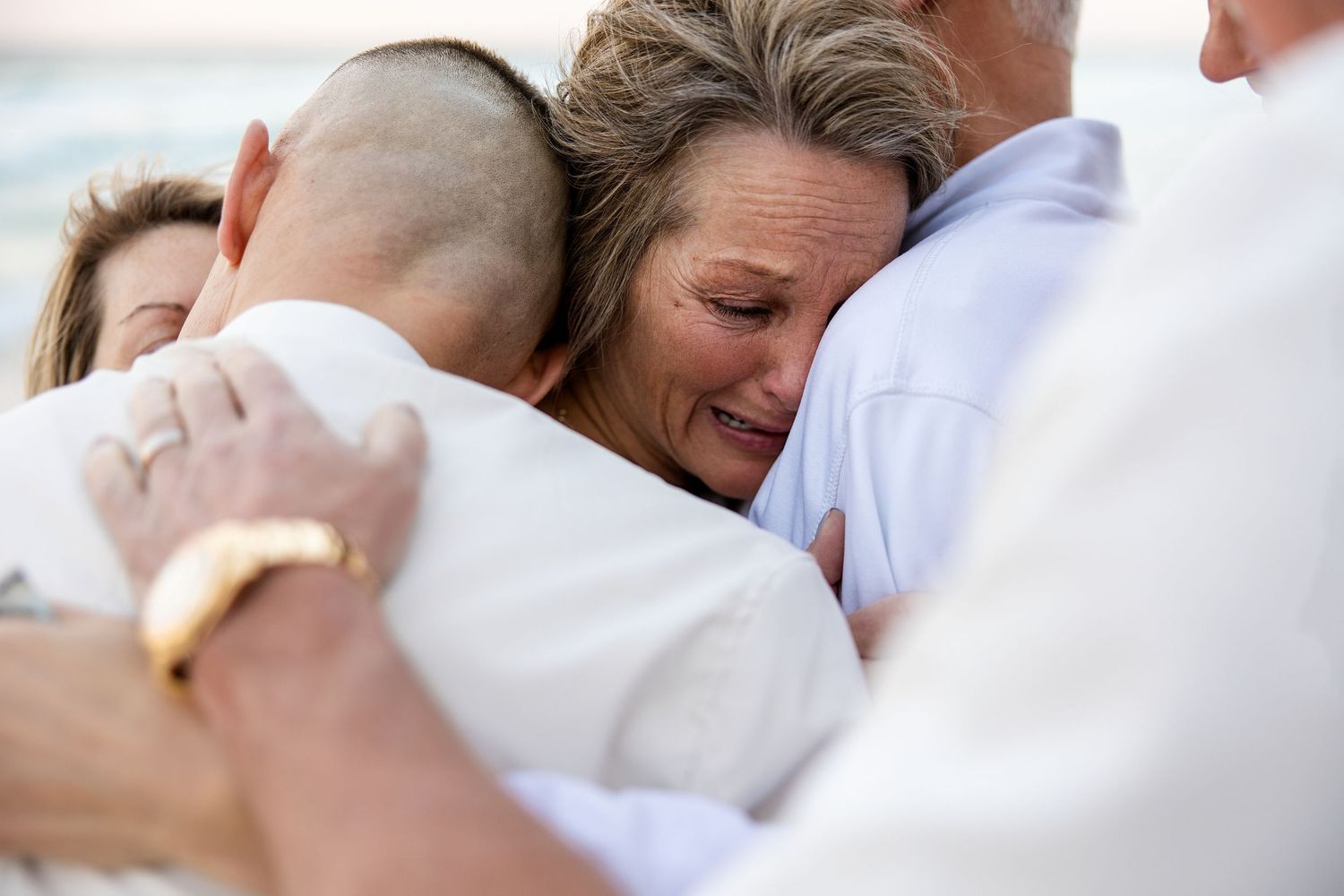 Emotional group hug among people dressed in white at a beach, capturing a heartfelt moment of joy and connection.