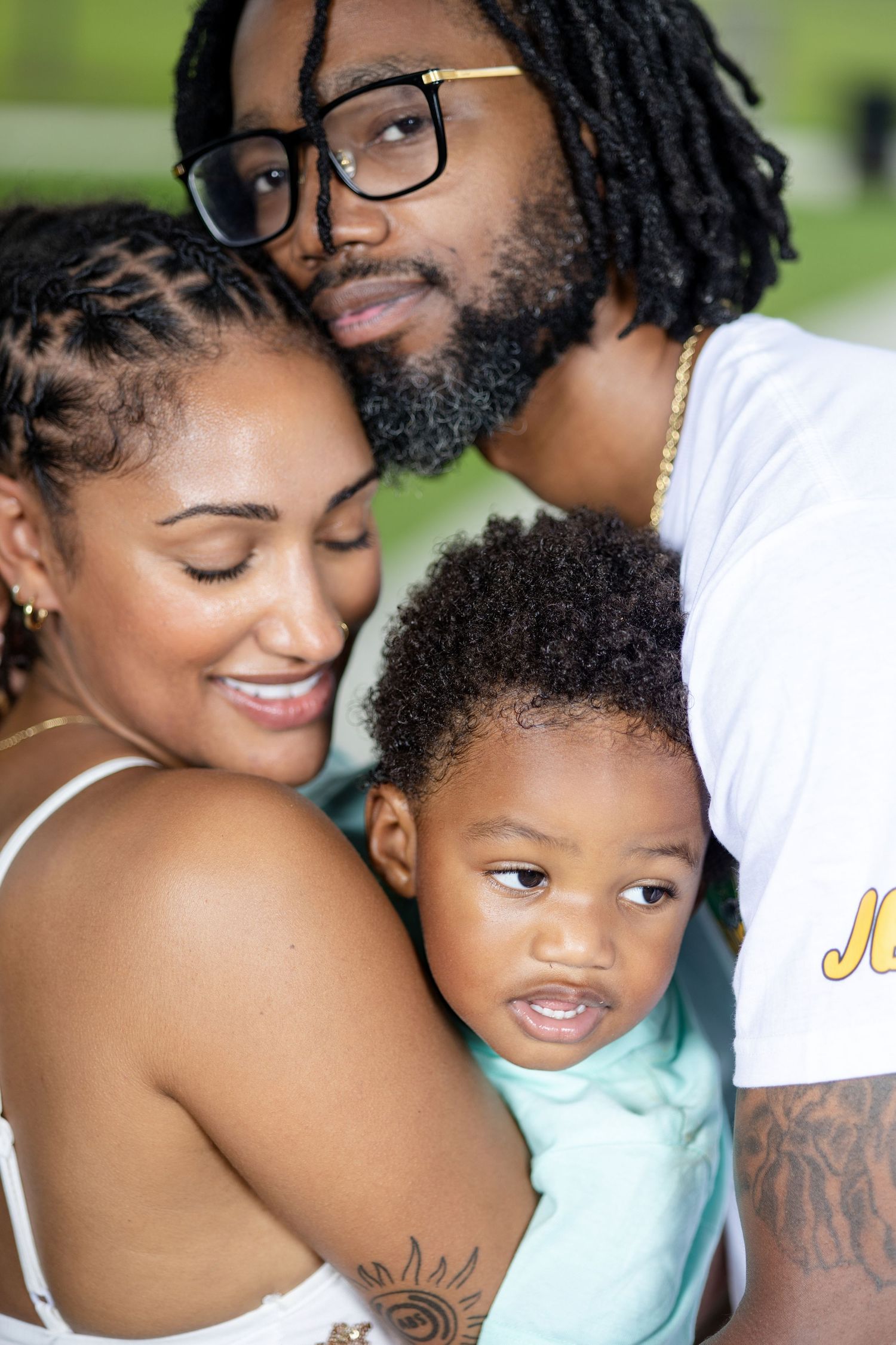 A loving family portrait of a couple and their young child embracing outdoors, smiling warmly together.