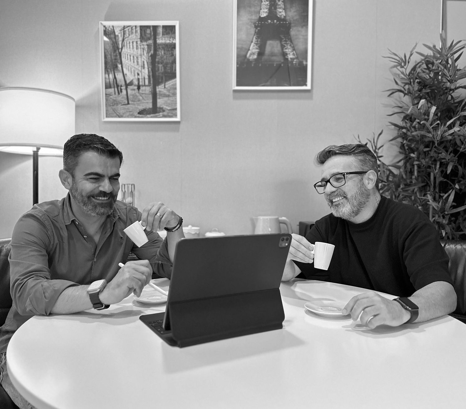 Two colleagues having coffee while looking at tablet during casual meeting.