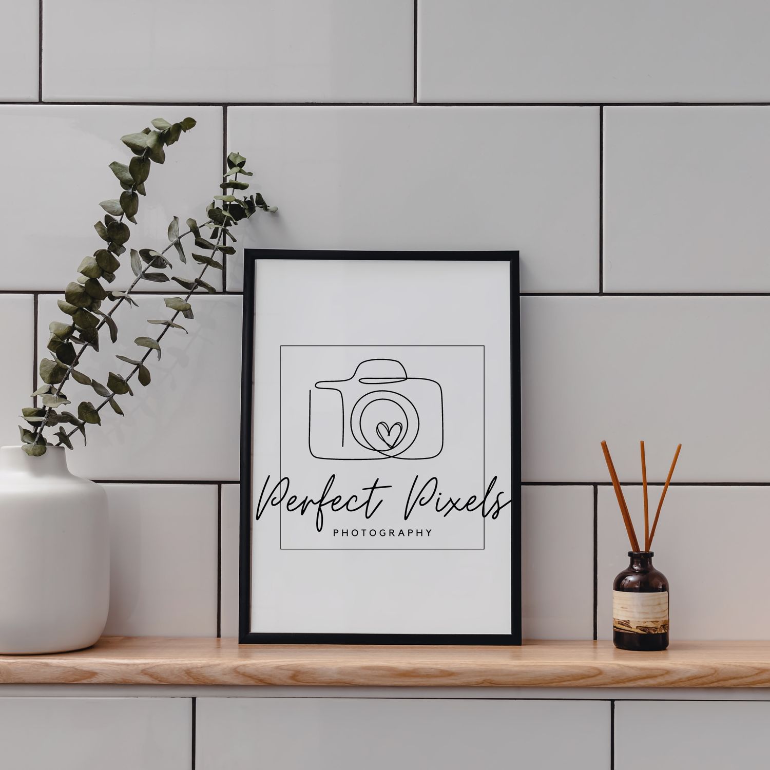 Minimalist photography branding display with framed logo, eucalyptus plant and home decor items.