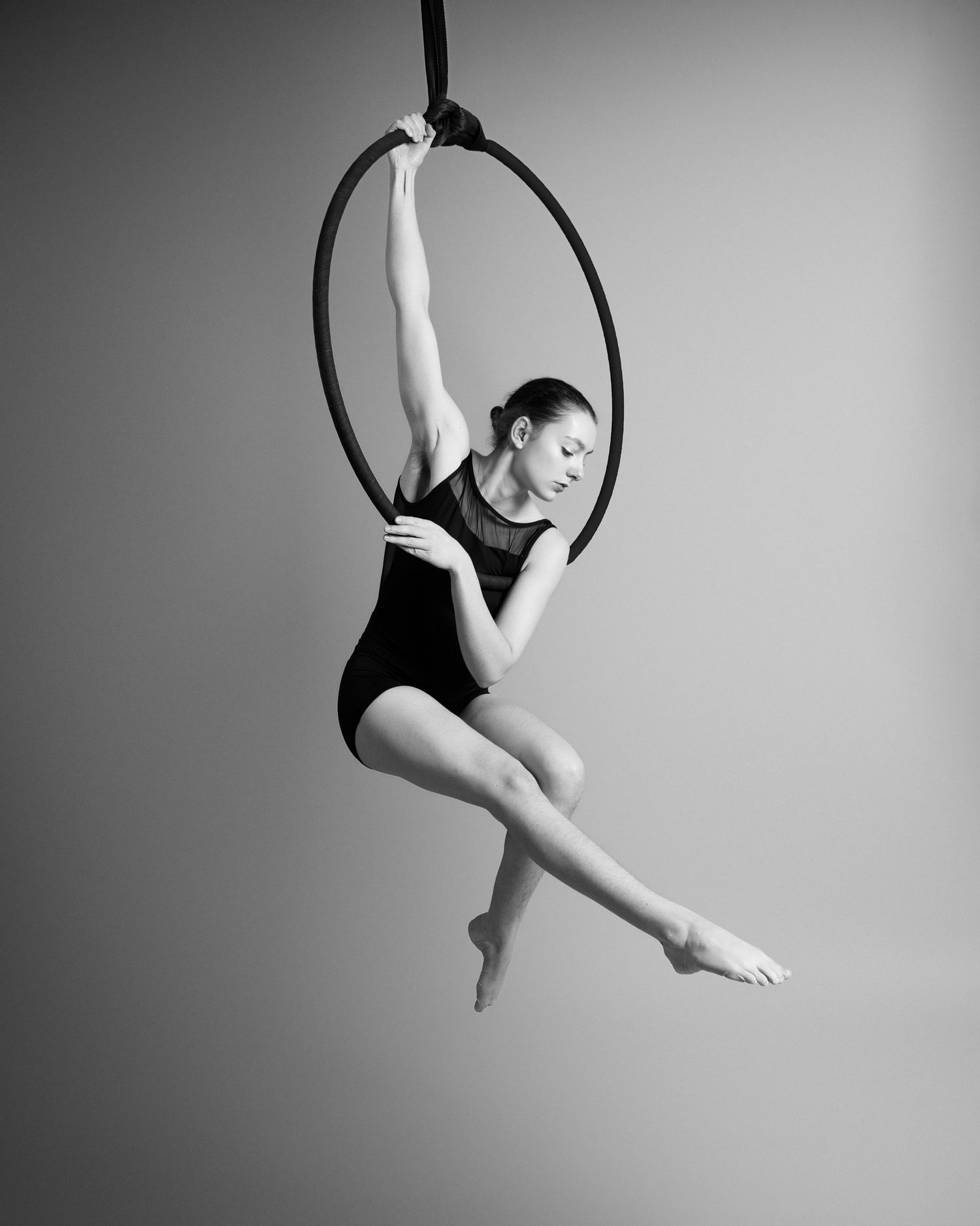 Graceful aerial dancer performs elegant movements on a suspended hoop against a monochromatic background.
