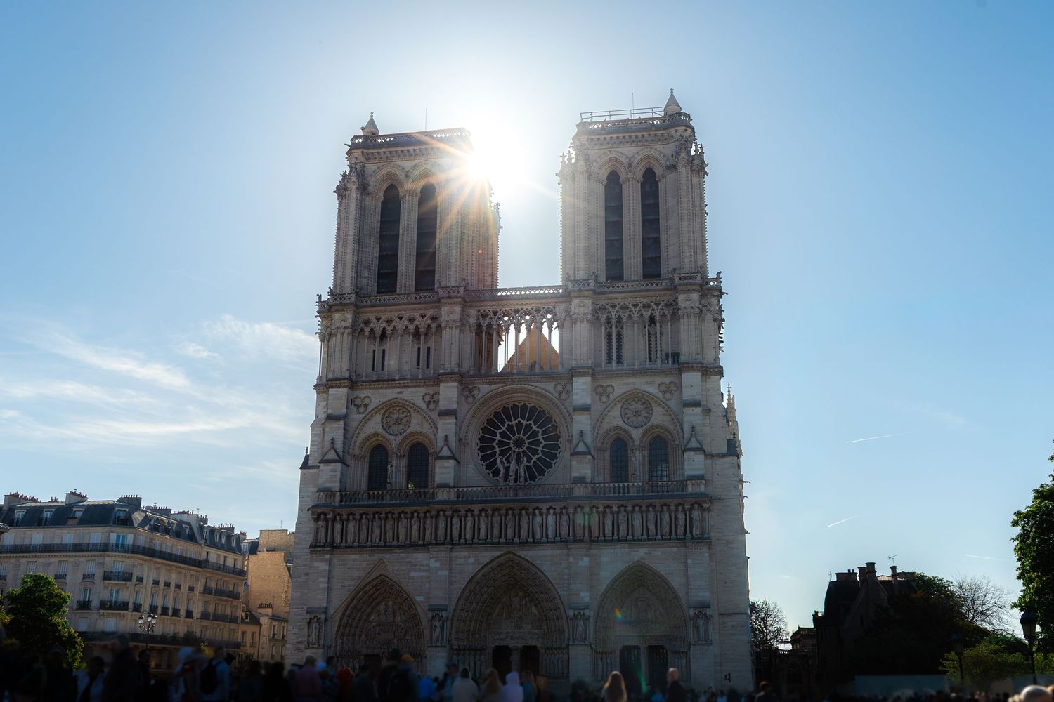 Notre-Dame Cathedral in Paris bathed in golden sunlight, showcasing its iconic Gothic facade and twin towers against a blue sky.