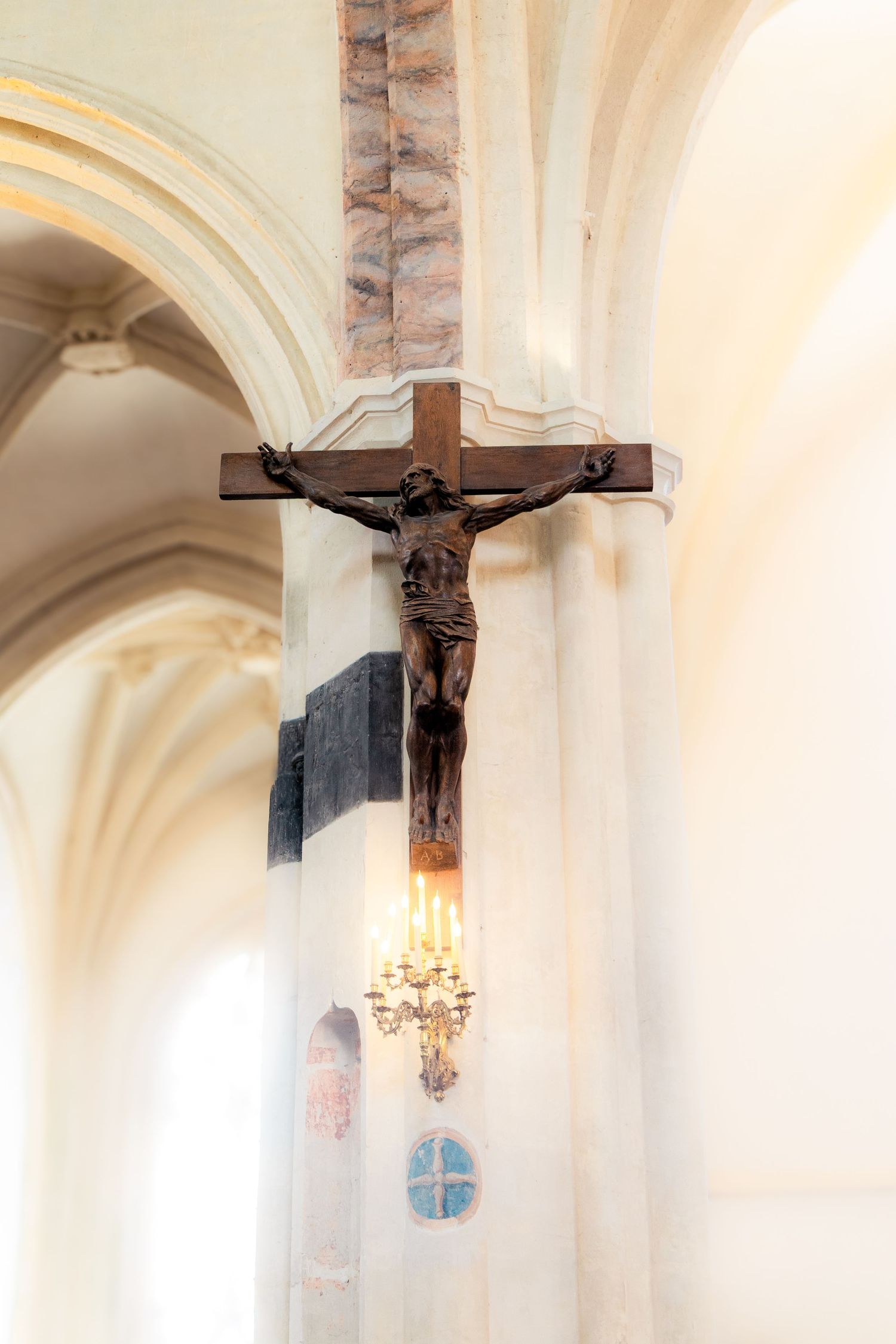 Wooden crucifix mounted on a white pillar inside a historic church with arched ceilings and candlelight.