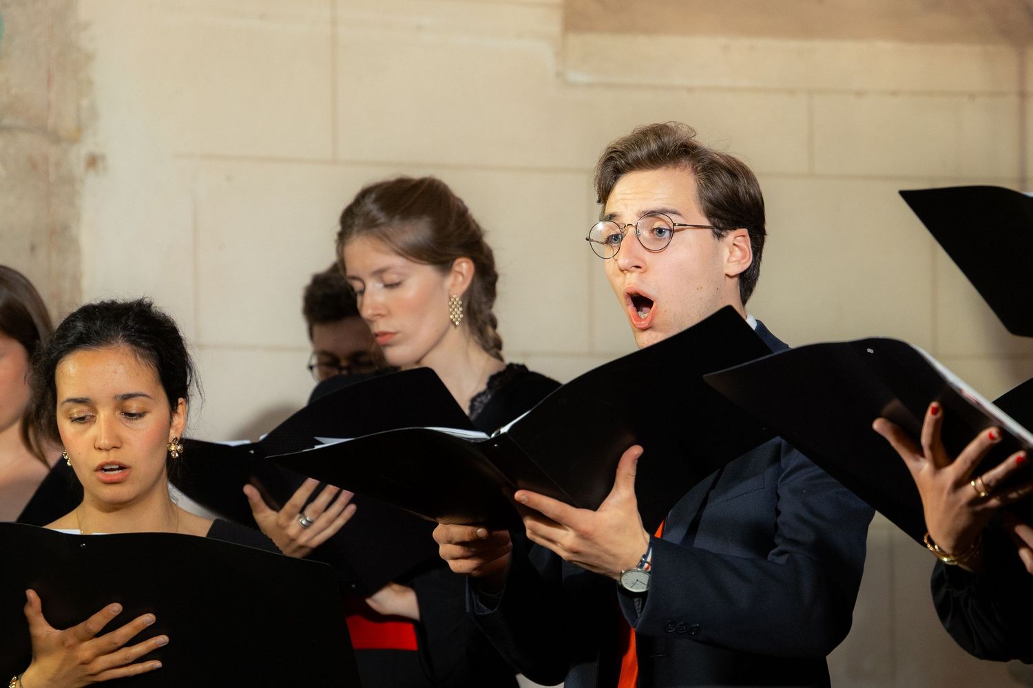 Young choir singers performing with black folders in a formal choral concert setting.