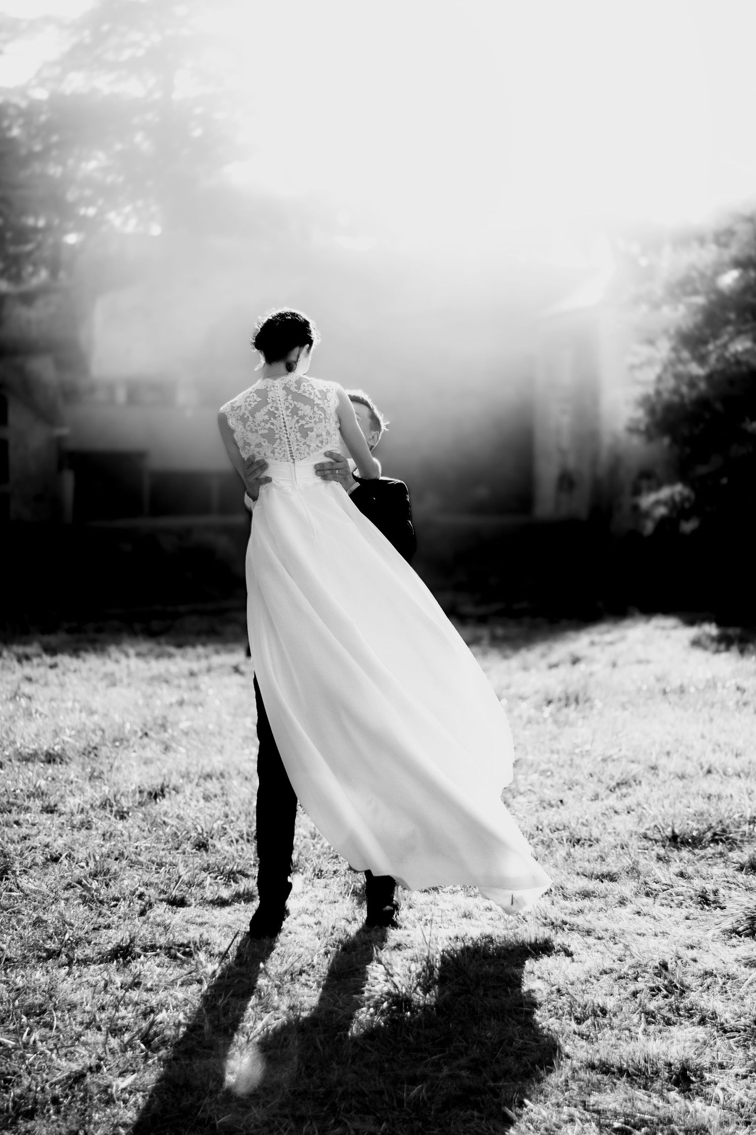 Black and white photo of bride and groom walking through misty outdoor venue, wedding dress flowing gracefully.