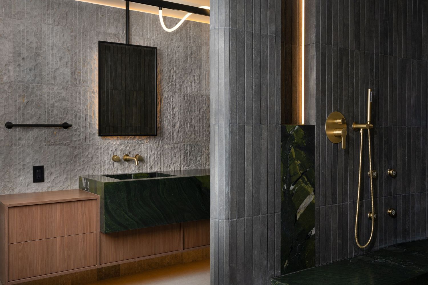 Luxury bathroom with green marble vanity, gold fixtures, pink wood cabinets, and dark slate shower walls.
