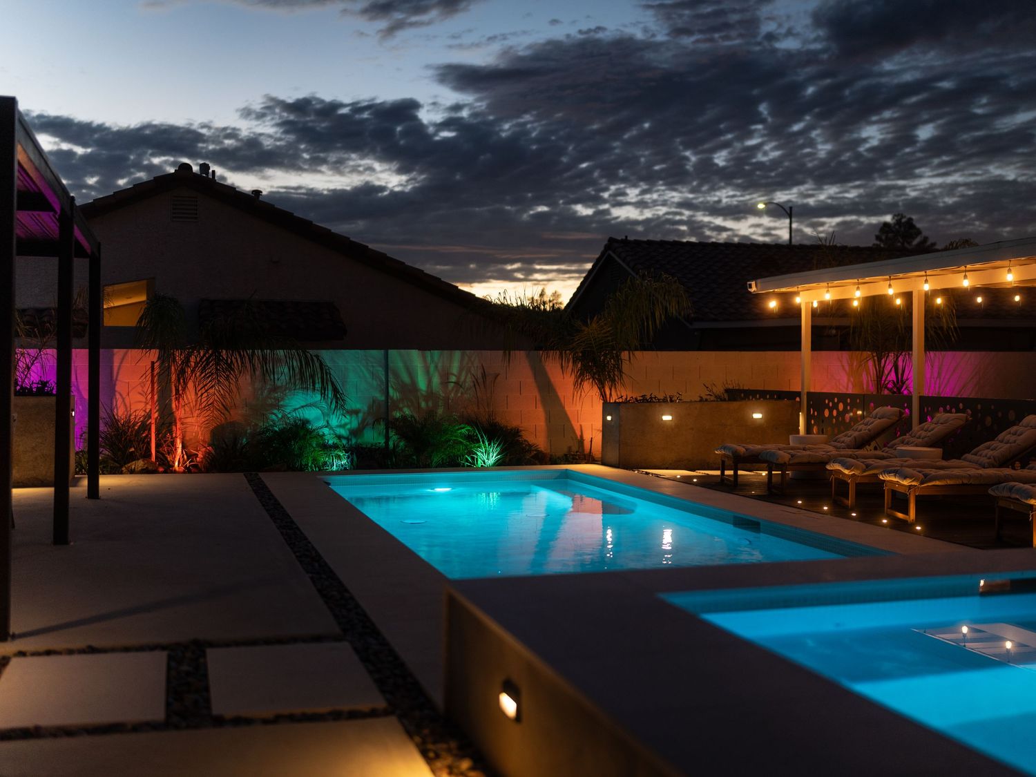Illuminated swimming pool at dusk with modern architectural features and ambient lighting creating a luxurious atmosphere.