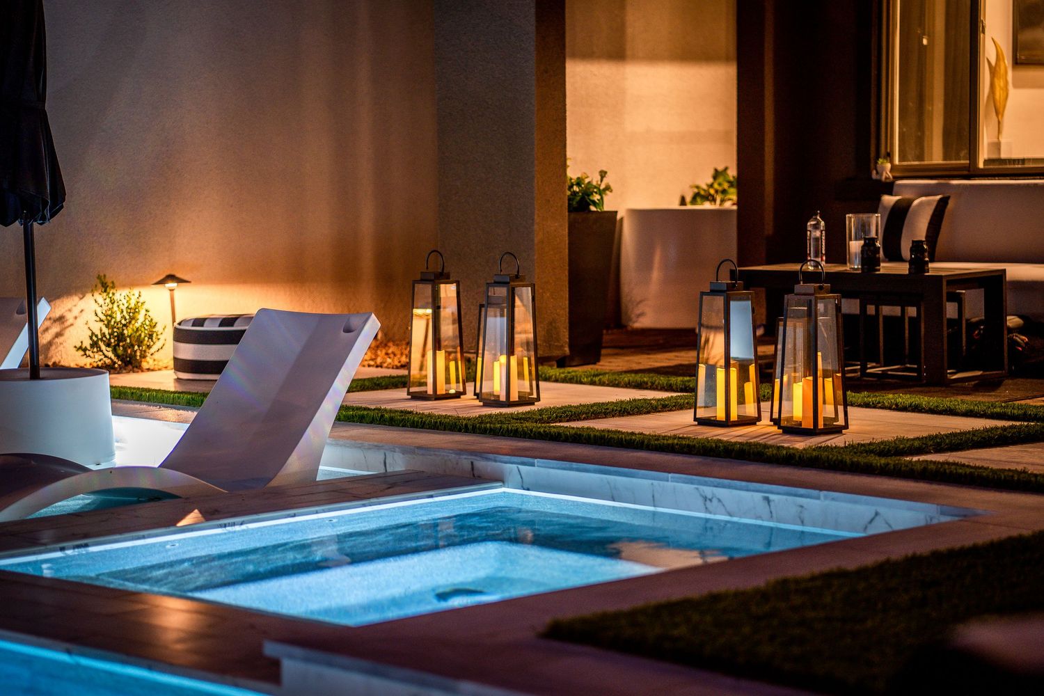 Modern poolside lounge area at night with illuminated water features and contemporary outdoor furniture.
