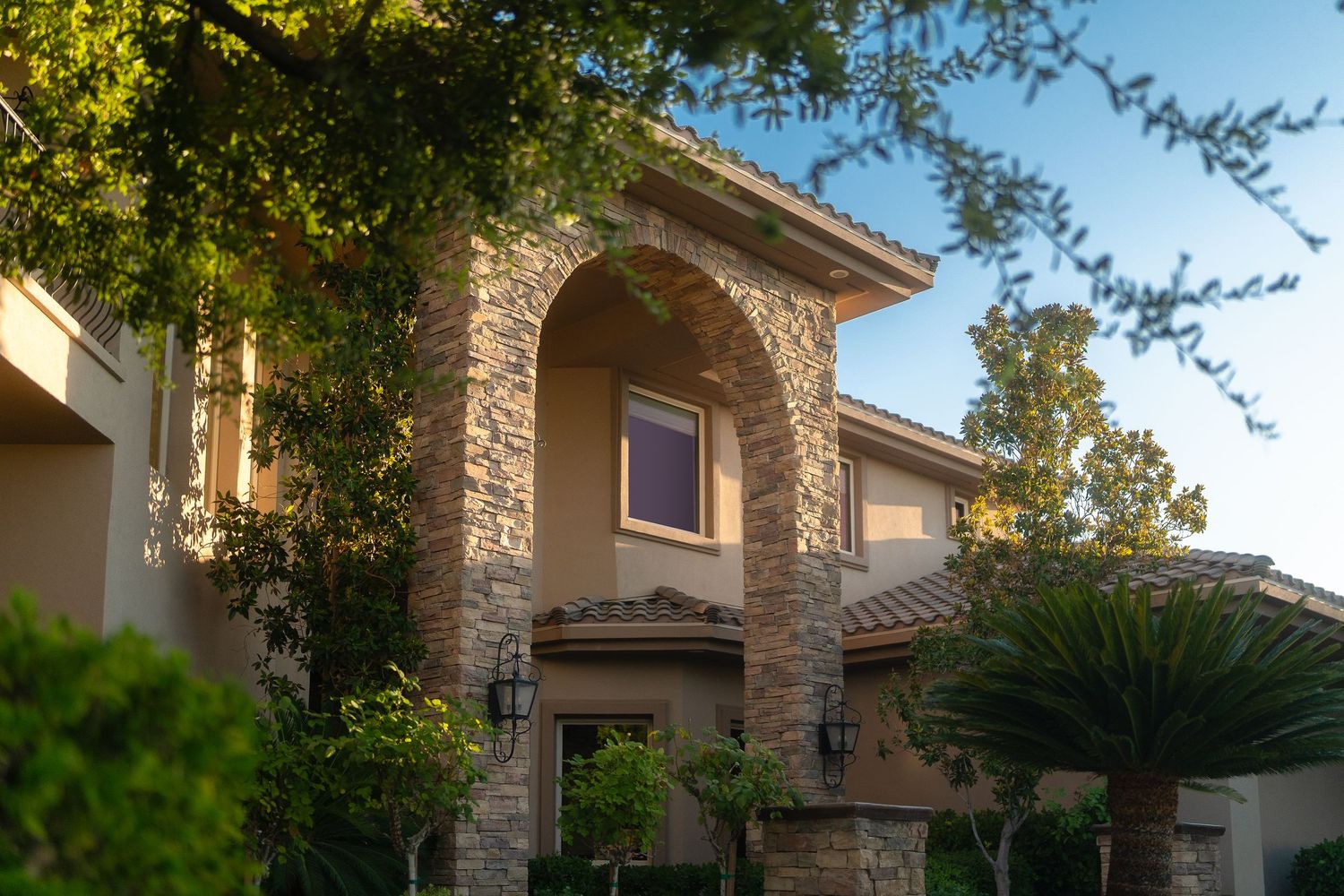 Mediterranean style luxury home exterior with stone accents and lush landscaping.