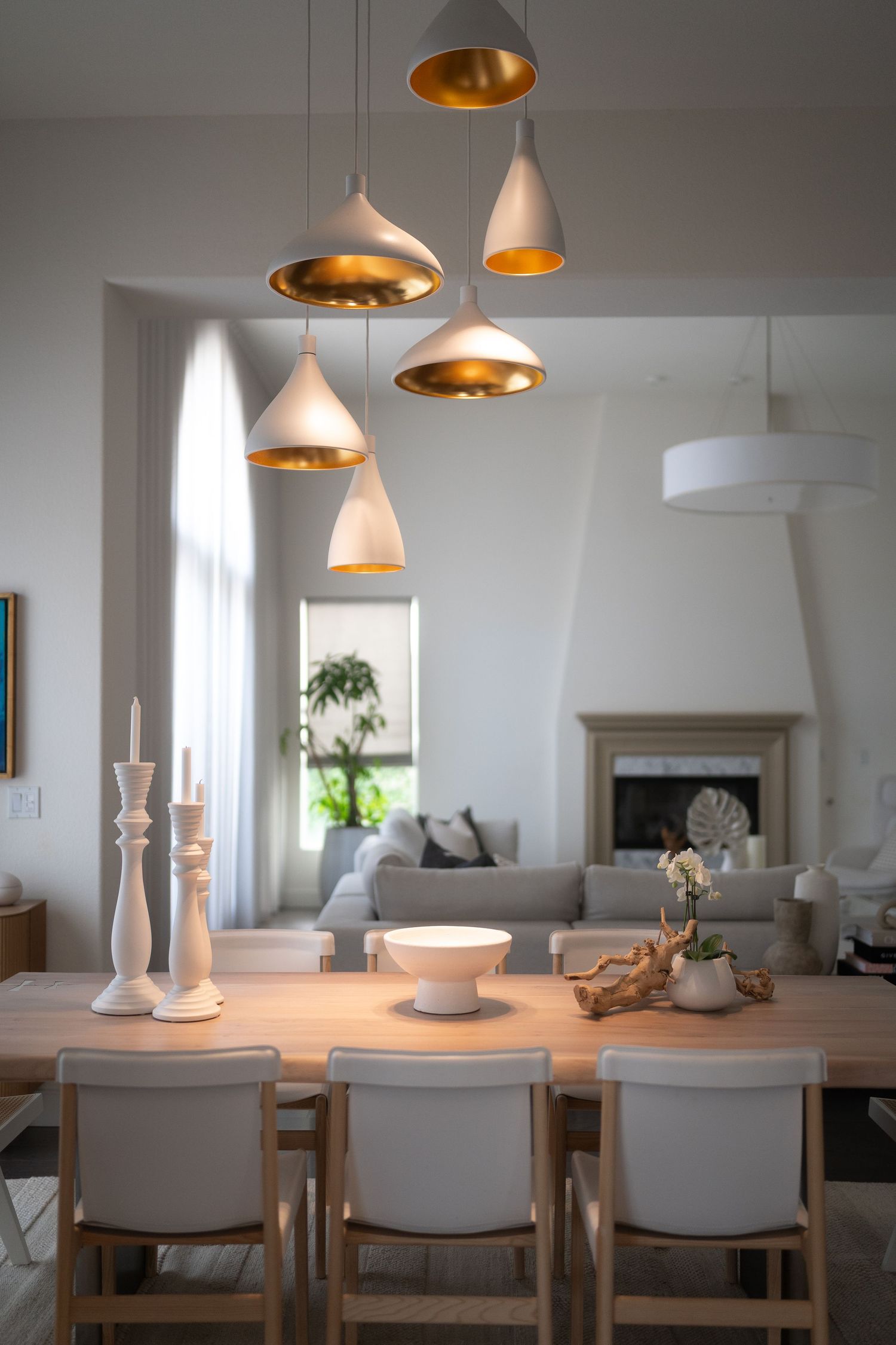 Elegant dining area with pendant lights featuring copper interiors and white modern chairs.