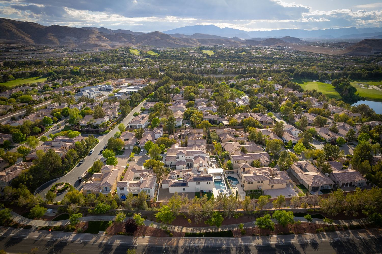 Aerial panorama of residential neighborhood with mountain ranges in the background under blue skies.