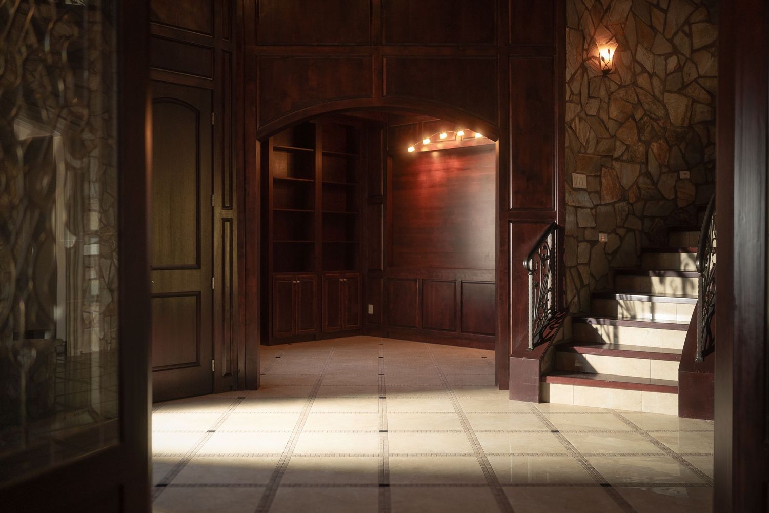 Dramatic stone hallway with warm lighting and arched doorways creates an elegant entrance atmosphere.