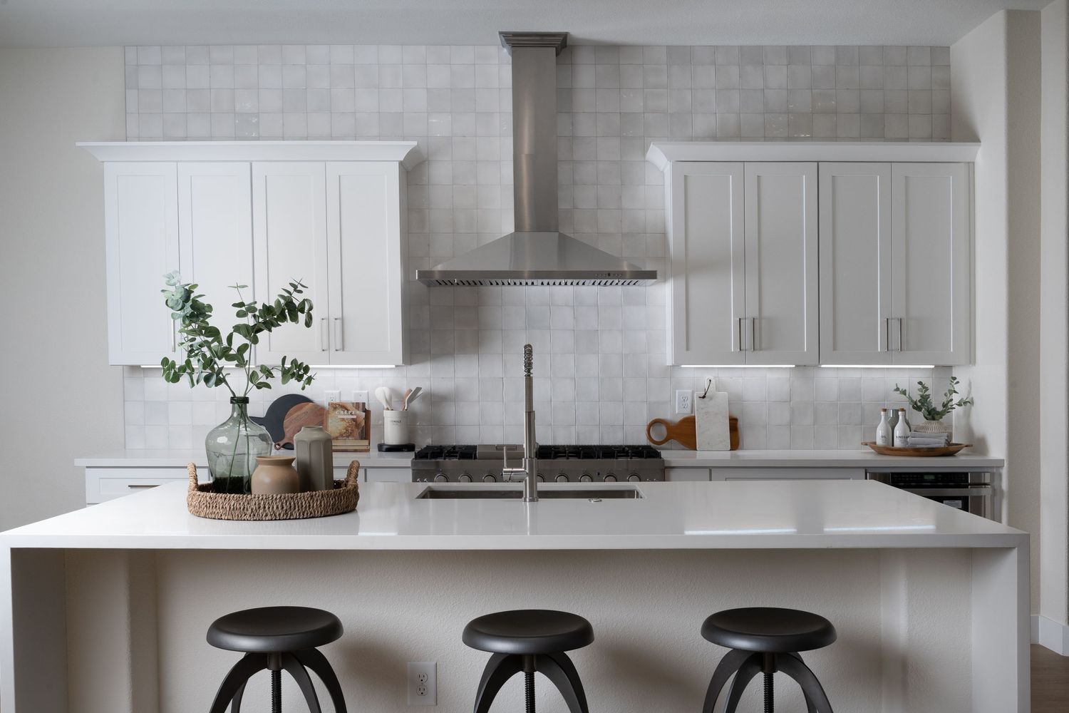 Modern white kitchen with sleek cabinets, quartz countertops, and black bar stools at the island.