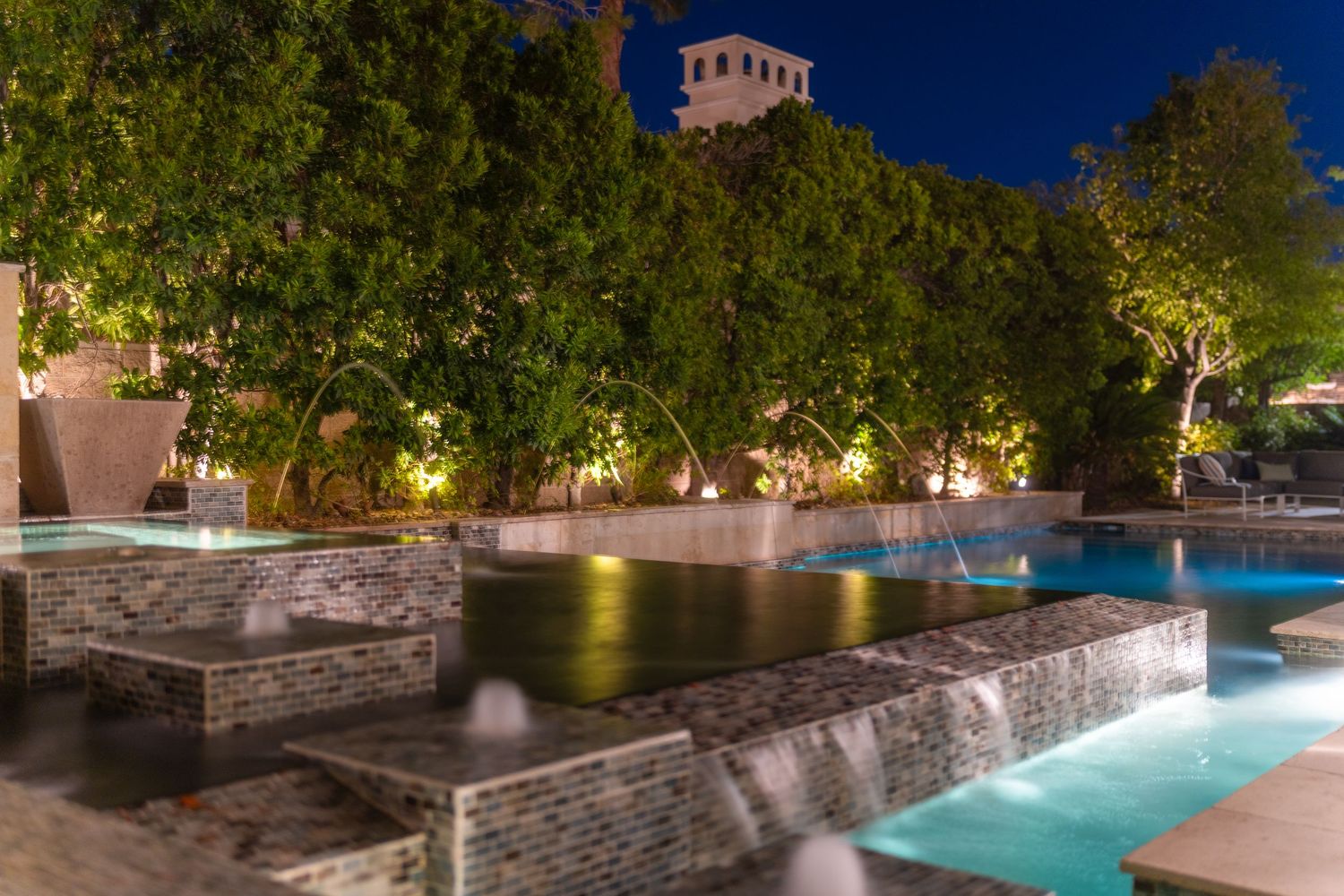 Illuminated swimming pool with stone walls and landscaping at night.