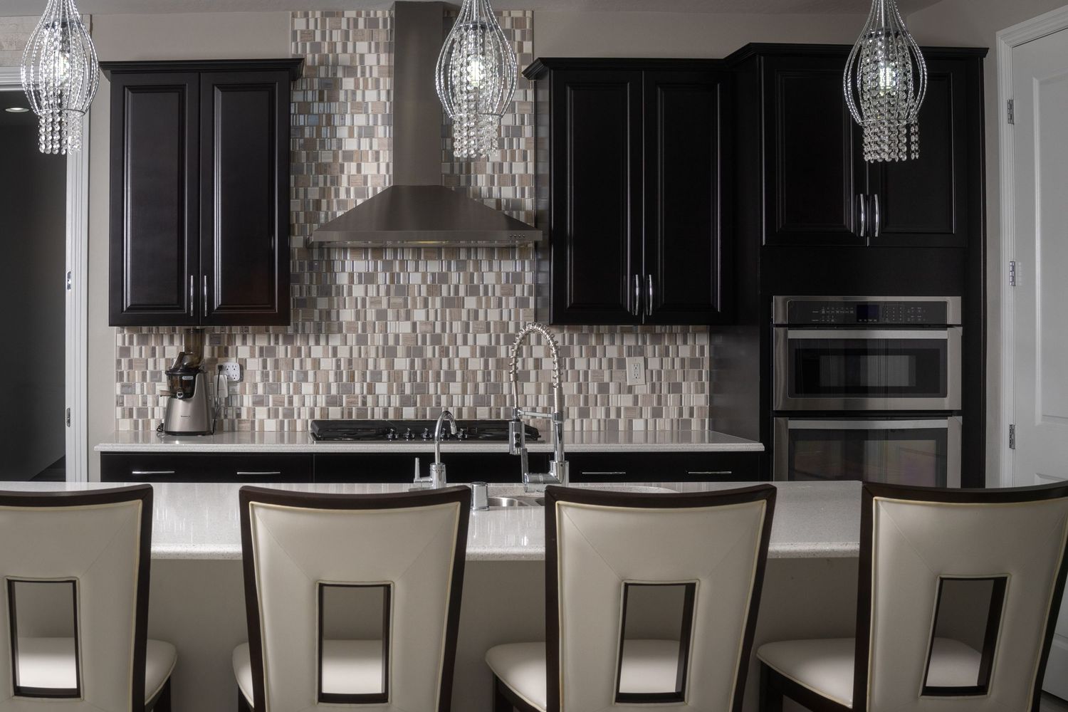 Modern kitchen with dark cabinets, mosaic tile backsplash, stainless steel appliances, and elegant pendant lights over island.