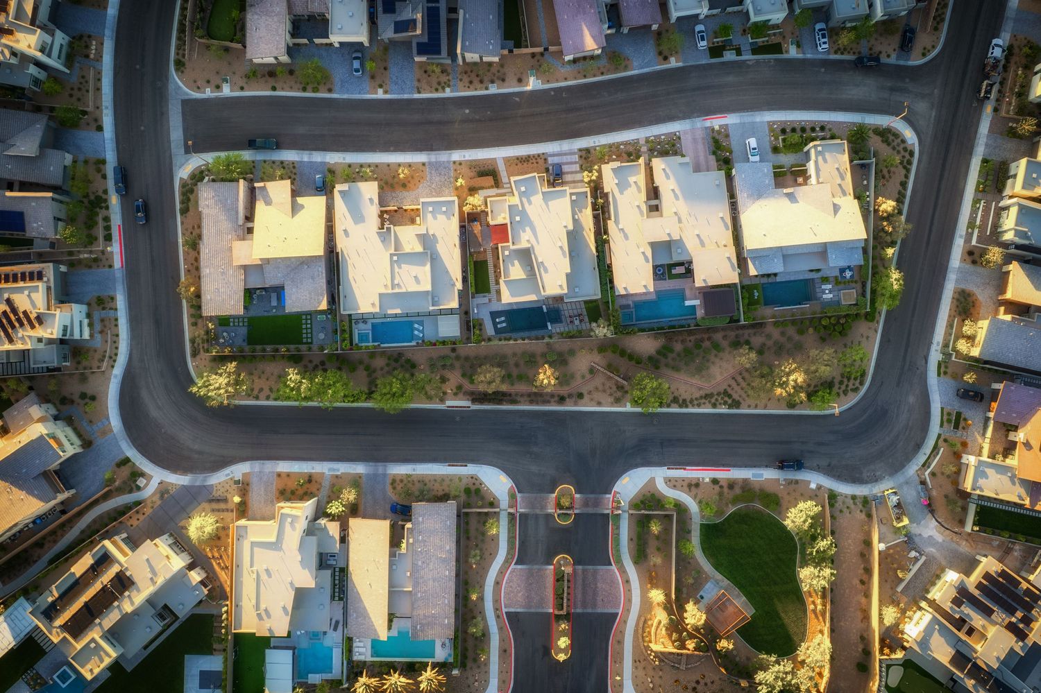 Aerial view of a modern suburban neighborhood with luxury homes, pools, and landscaped streets at dusk.