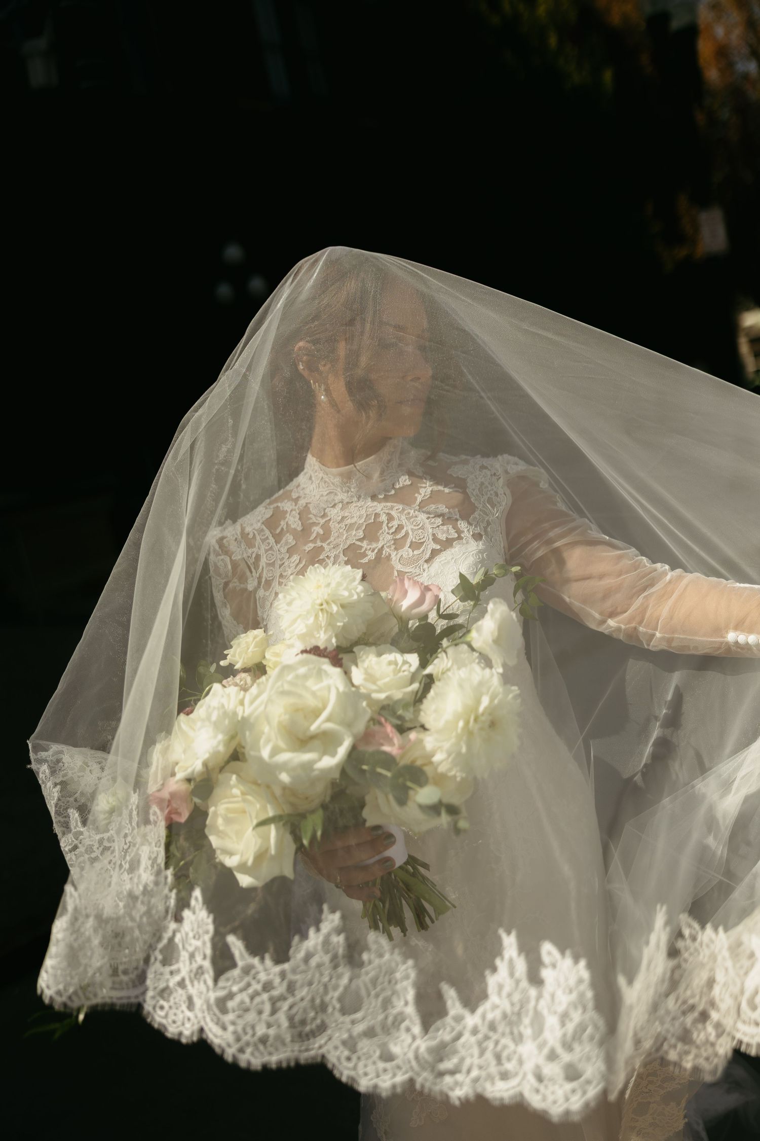 Close-up detail of delicate white lace veil with floral embellishments against a dark background.