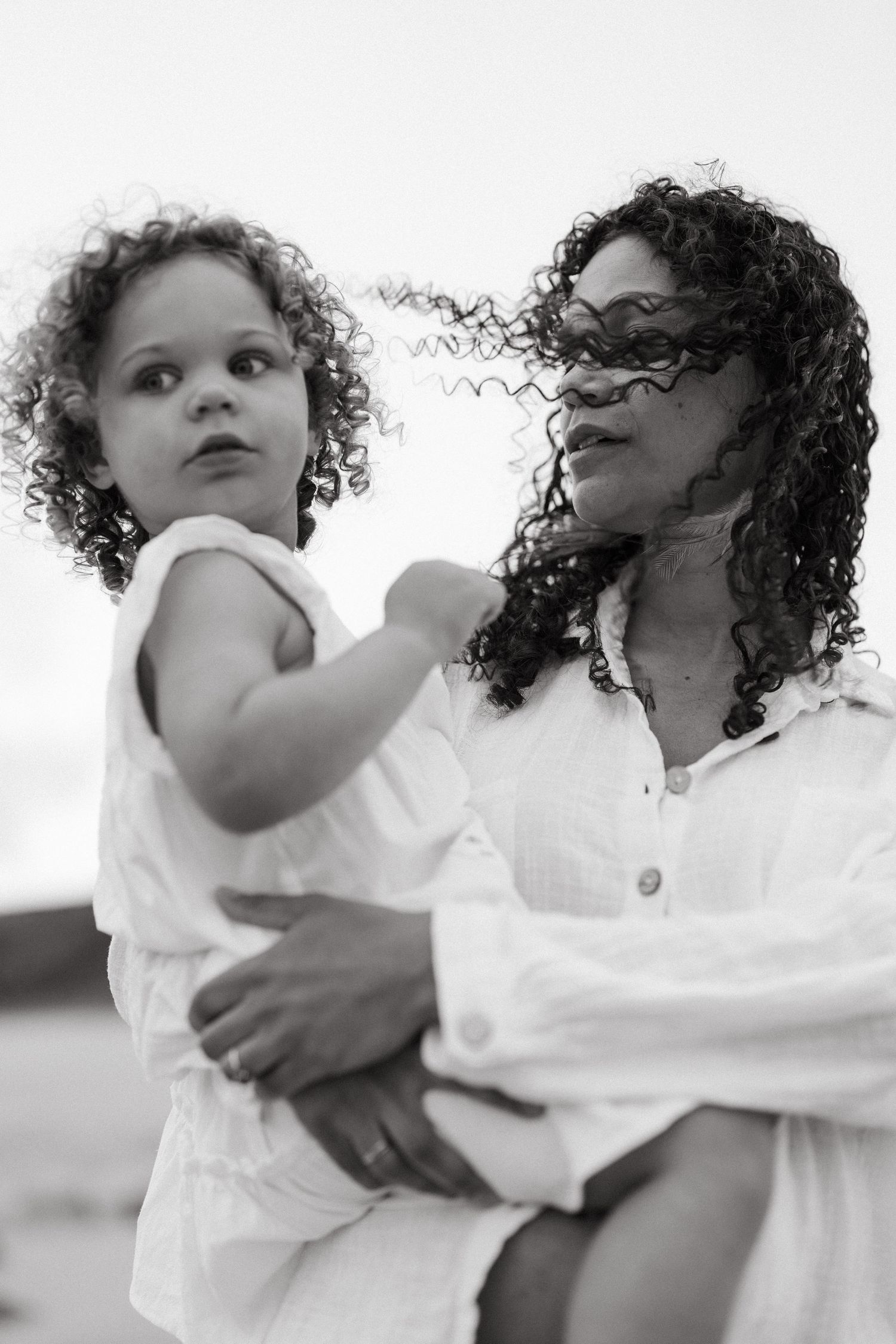 A series of black and white images showing tender moments between a parent and child with curly hair against a light background.