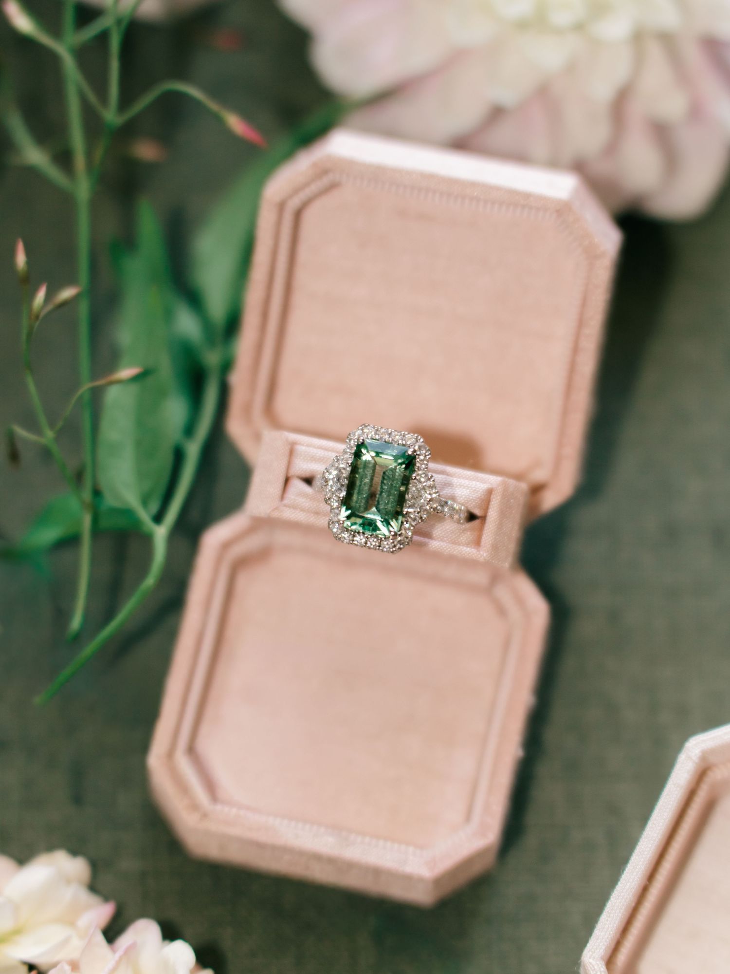 Vintage-style engagement ring in blush pink velvet box showcasing emerald cut center stone.