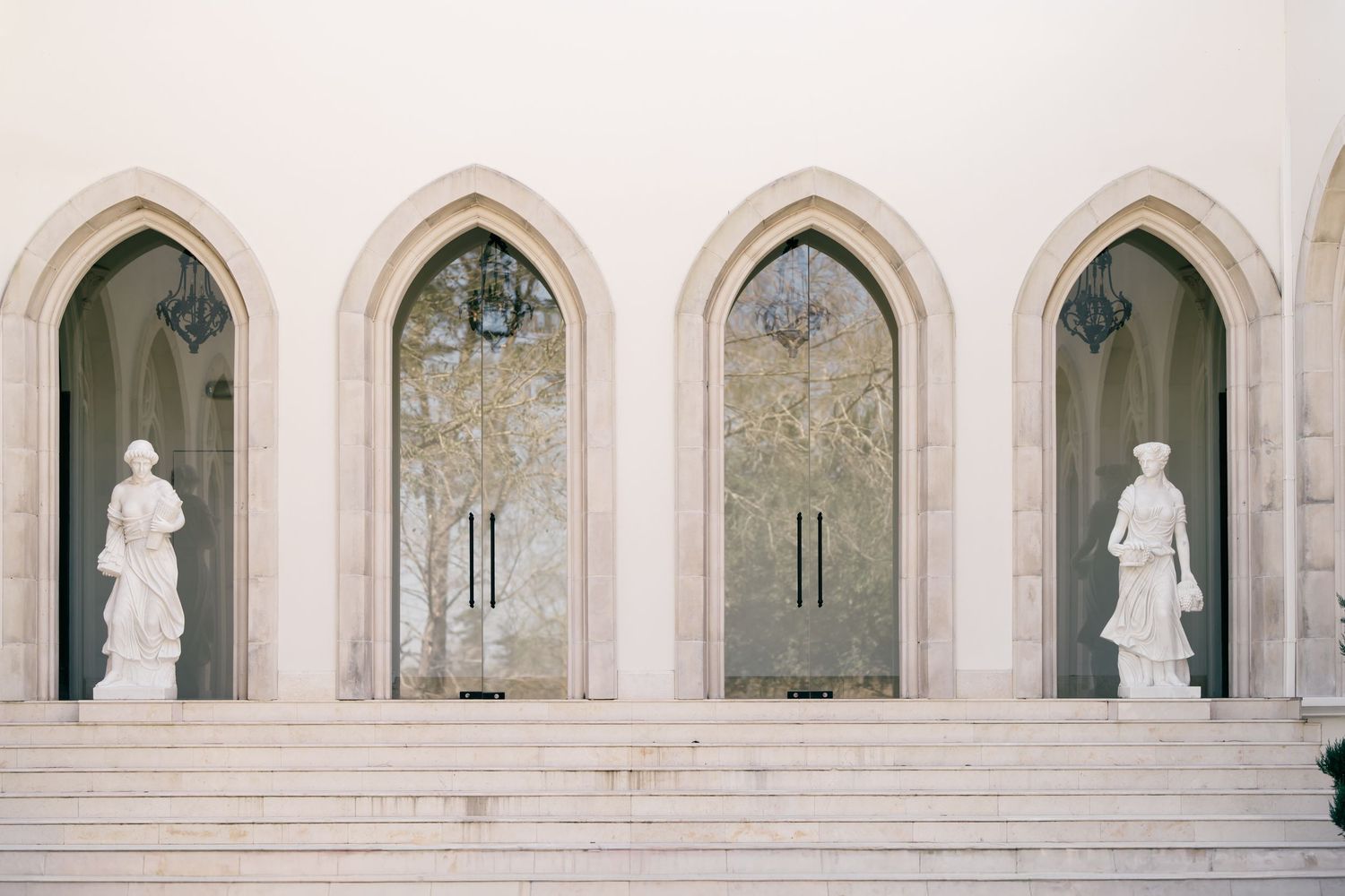 Elegant white marble statues stand in Gothic-style arched alcoves along a stone facade with ornate architectural details.