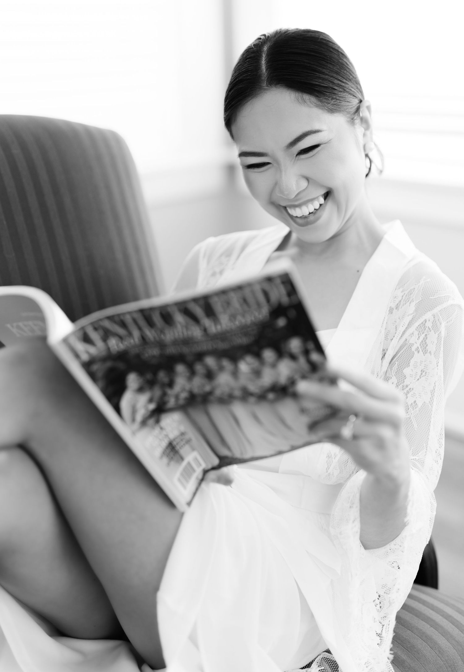 Person in white robe smiles while reading a magazine in a chair.