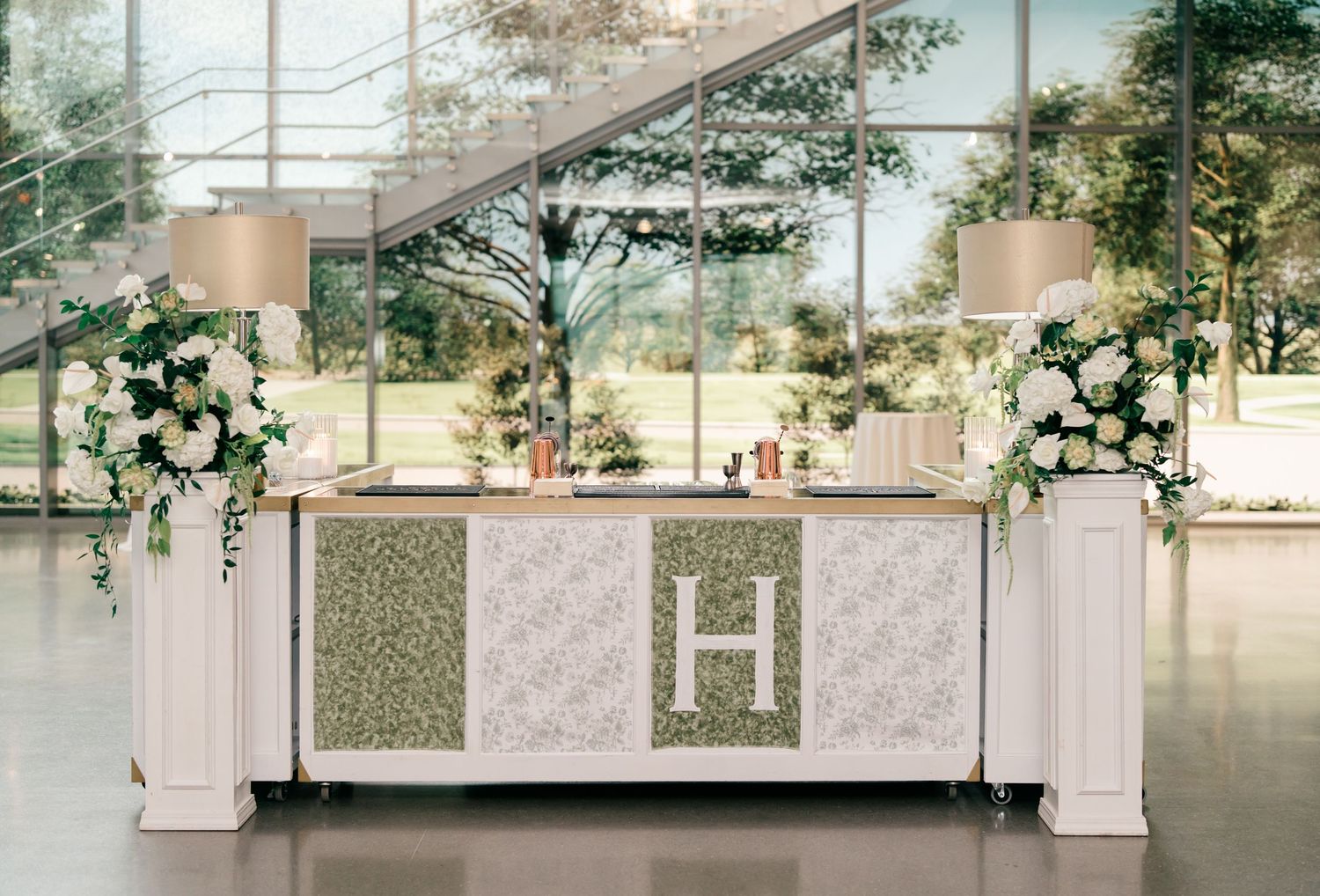 Green foliage decorates a modern indoor space with white columns and glass panels creating an elegant walkway.