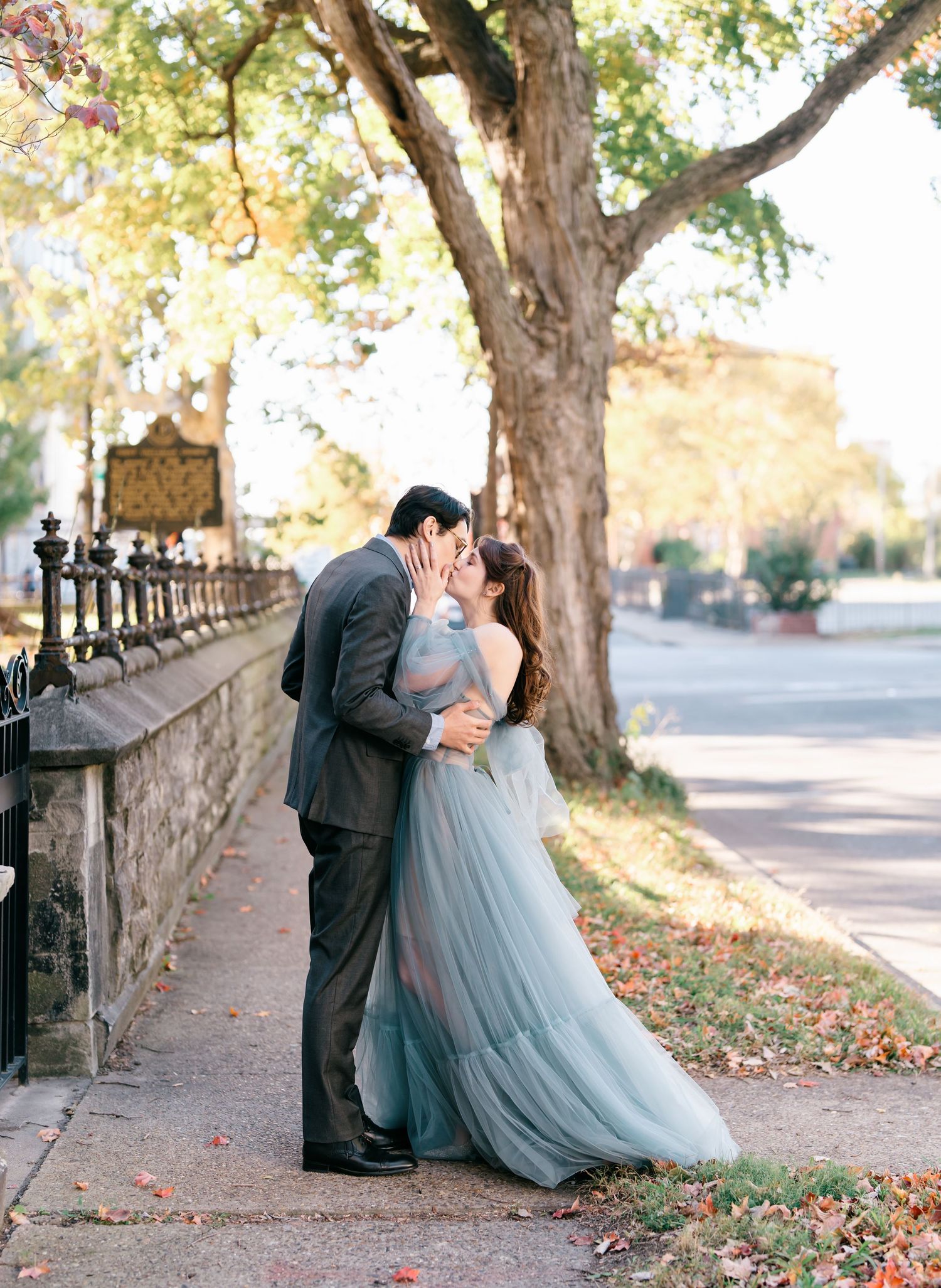 A romantic couple in formal attire share an intimate moment on stone steps surrounded by autumn trees.