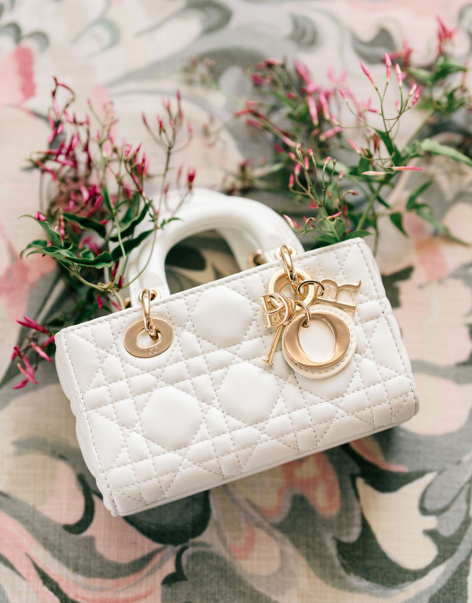 Elegant white quilted leather handbag with gold ring hardware details displayed against floral background.