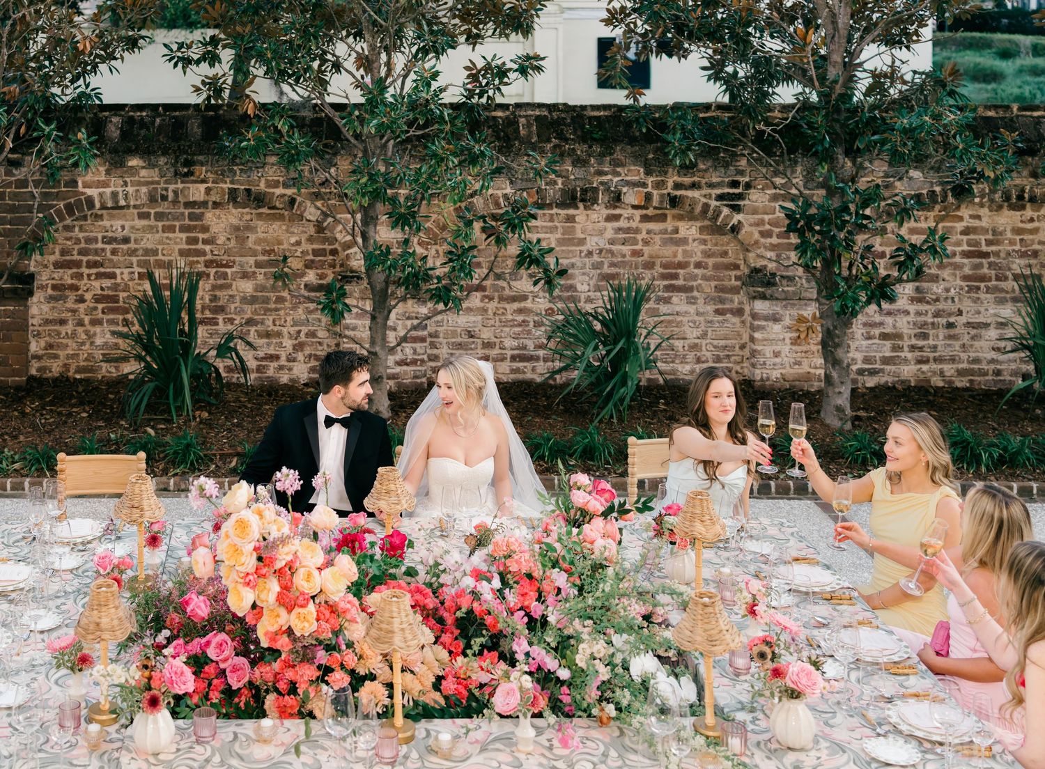 A panoramic view of a rustic brick wall decorated with colorful floral arrangements and candles for an outdoor event.