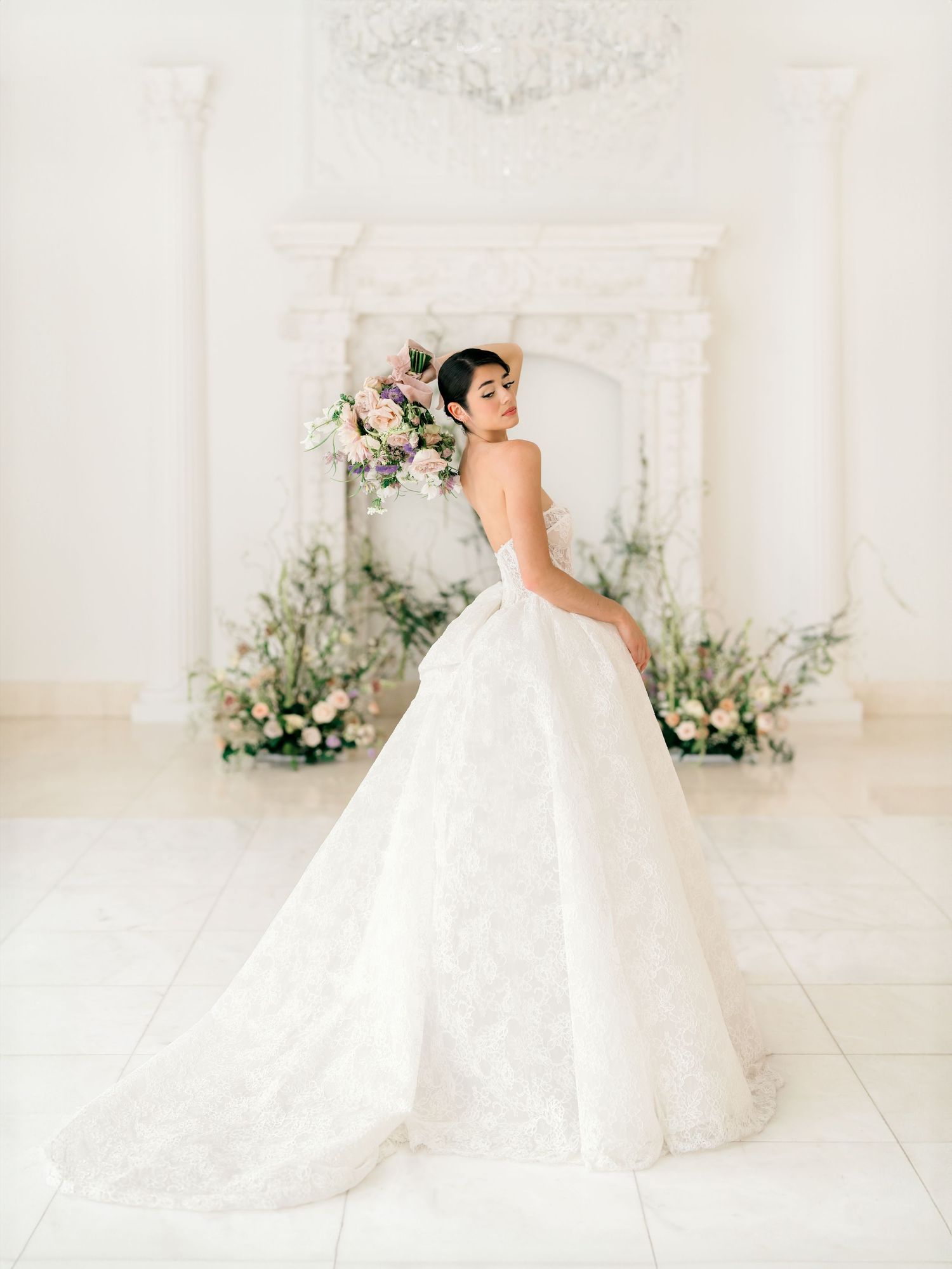 A flowing white ballgown wedding dress displayed in an elegant light-filled room with ornate decor.