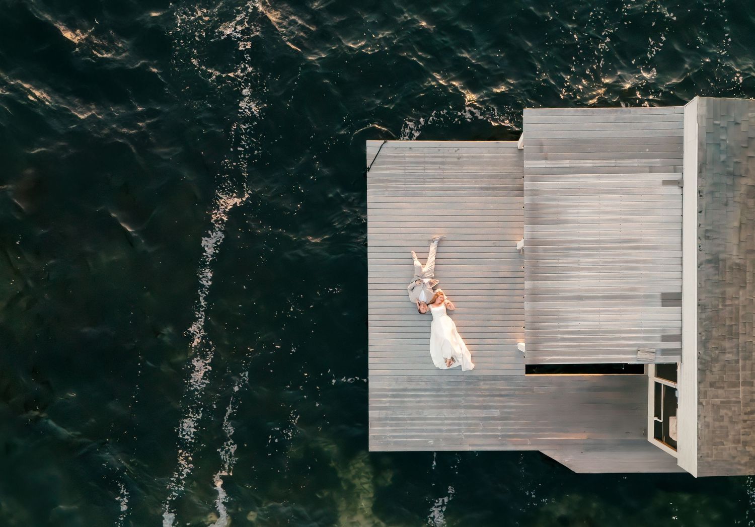 A drone portrait of a bride and groom laying on dock while the ocean waves surround them. Orlando, Florida real wedding.