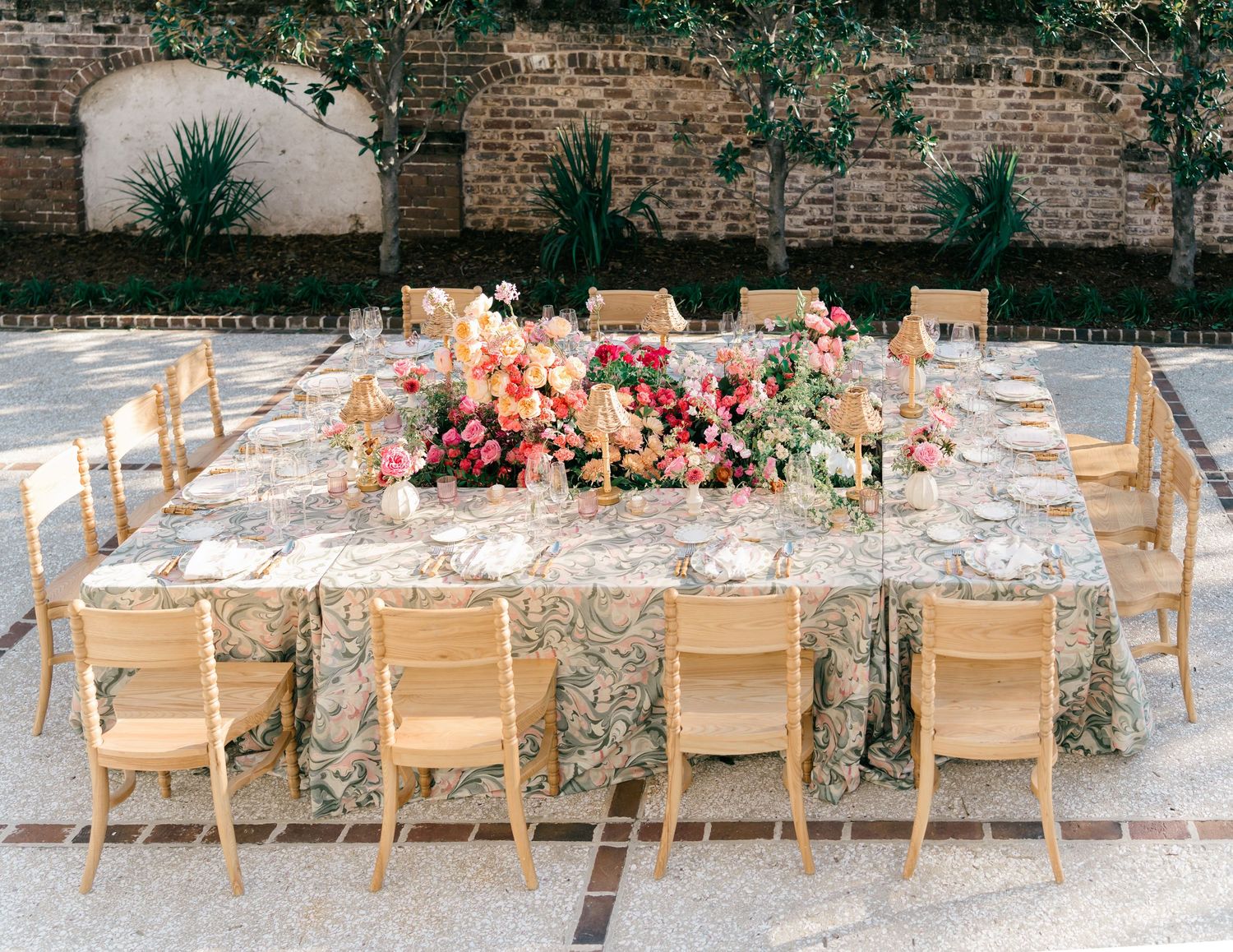 Long rustic dining tables set up outdoors with light wooden chairs and floral decorations.