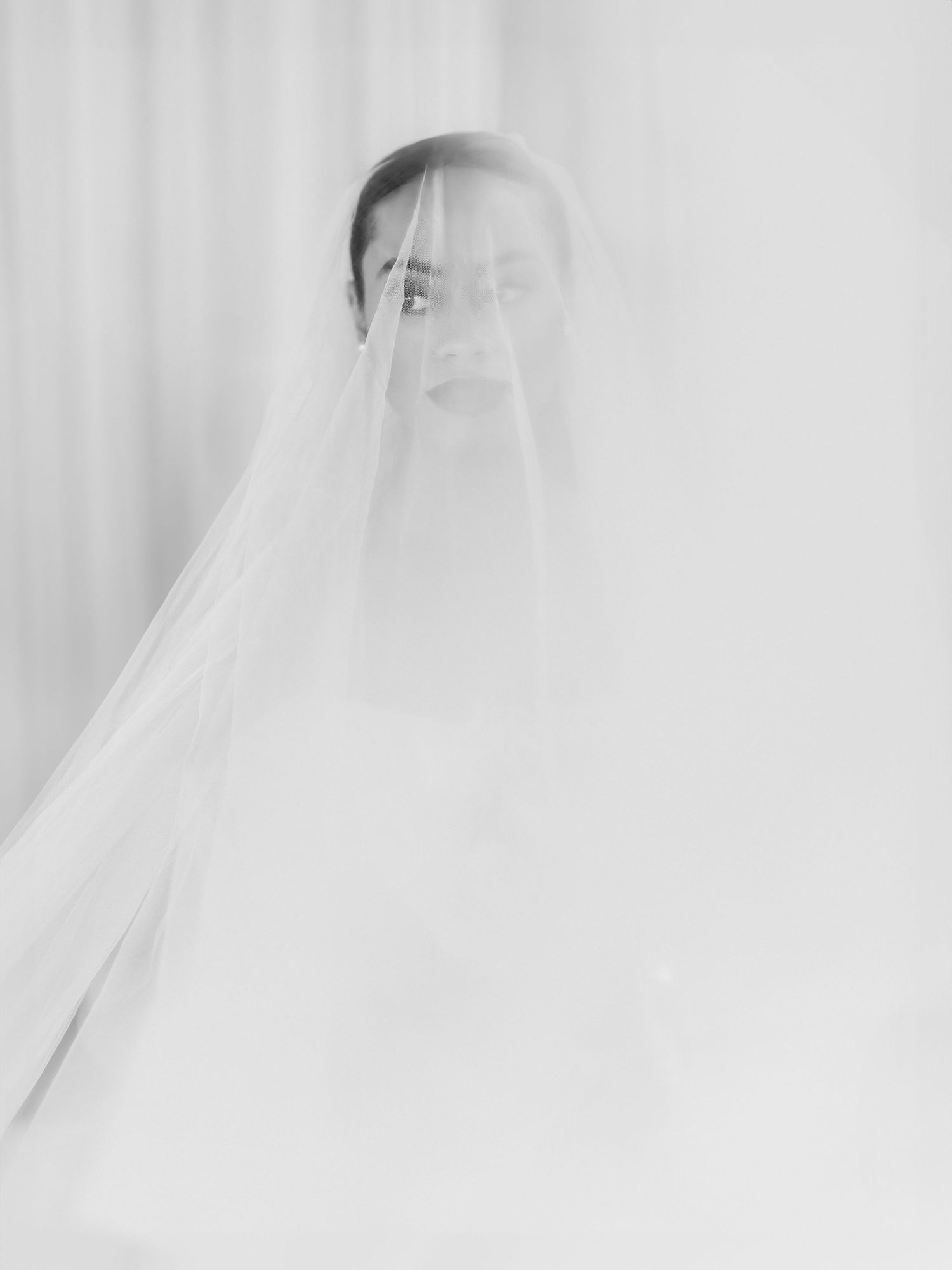 Black and white bridal portrait with sheer veil draped over face, ethereal and elegant wedding photography.
