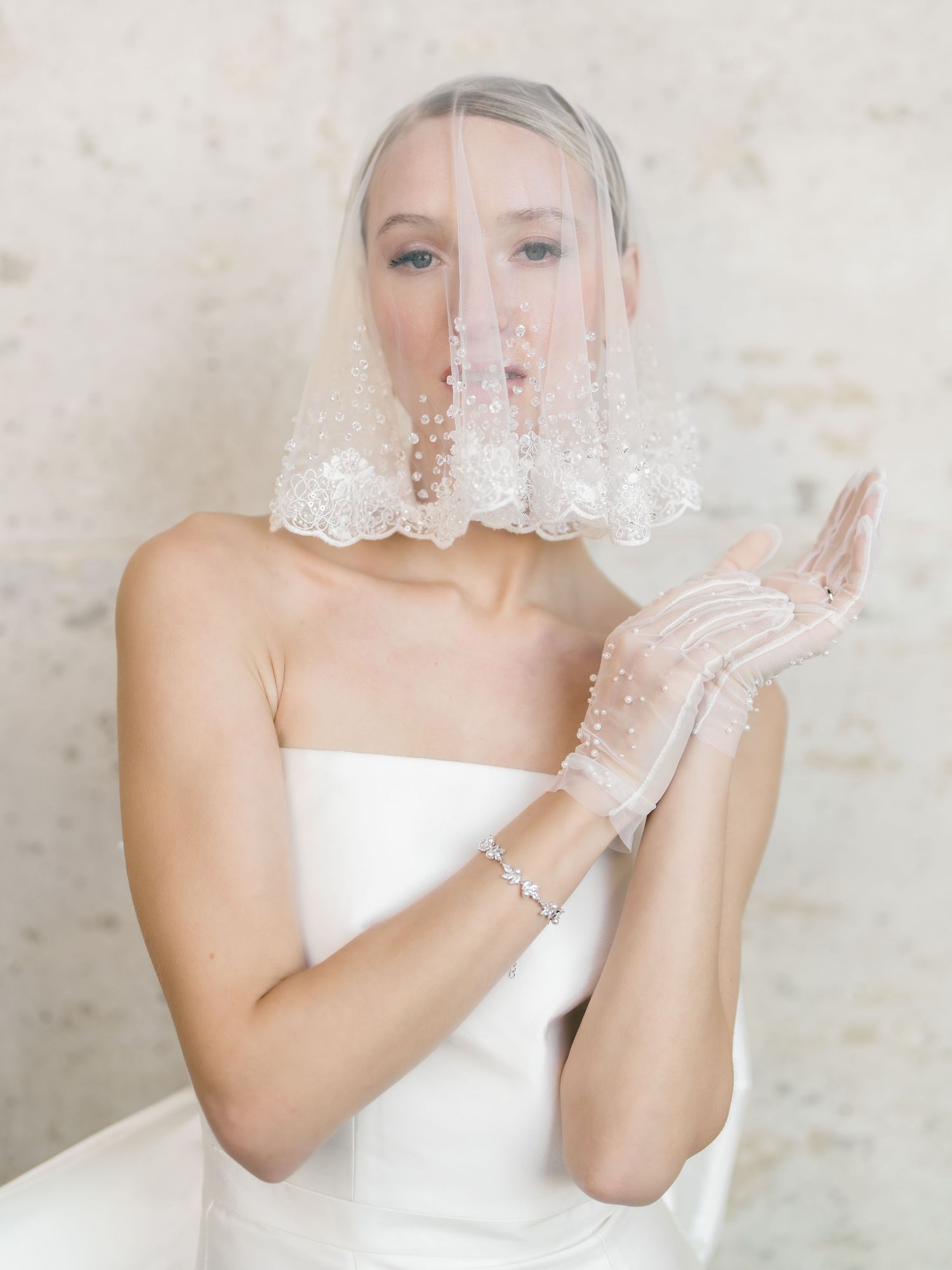 A bride in a white wedding dress plays with delicate lace veil material in a series of romantic portrait poses.
