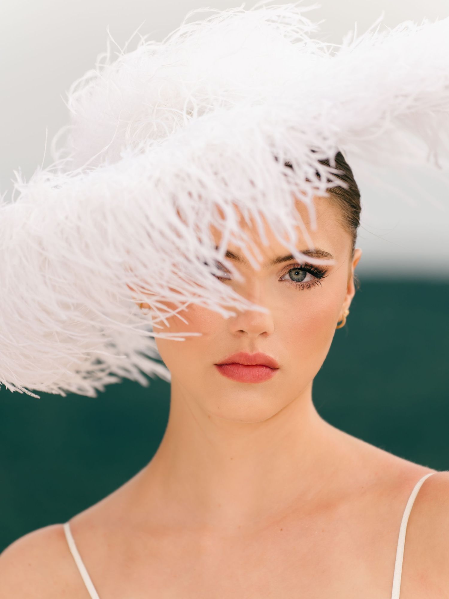 Close-up of bride wearing dramatic white feather headpiece with coral lips and blue eyes.