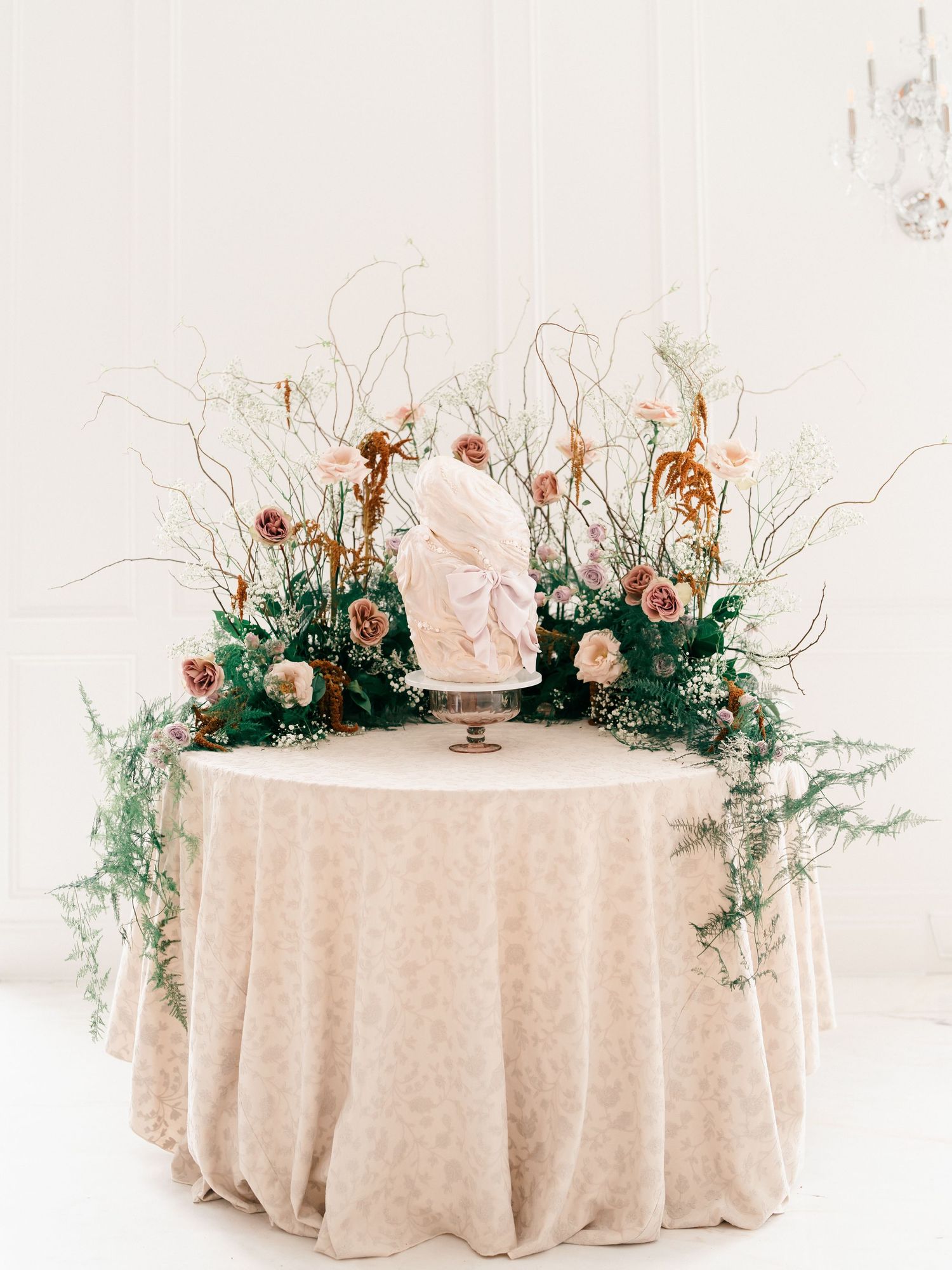 Elegant round tables with cream lace tablecloths decorated with soft pink roses and greenery arrangements.