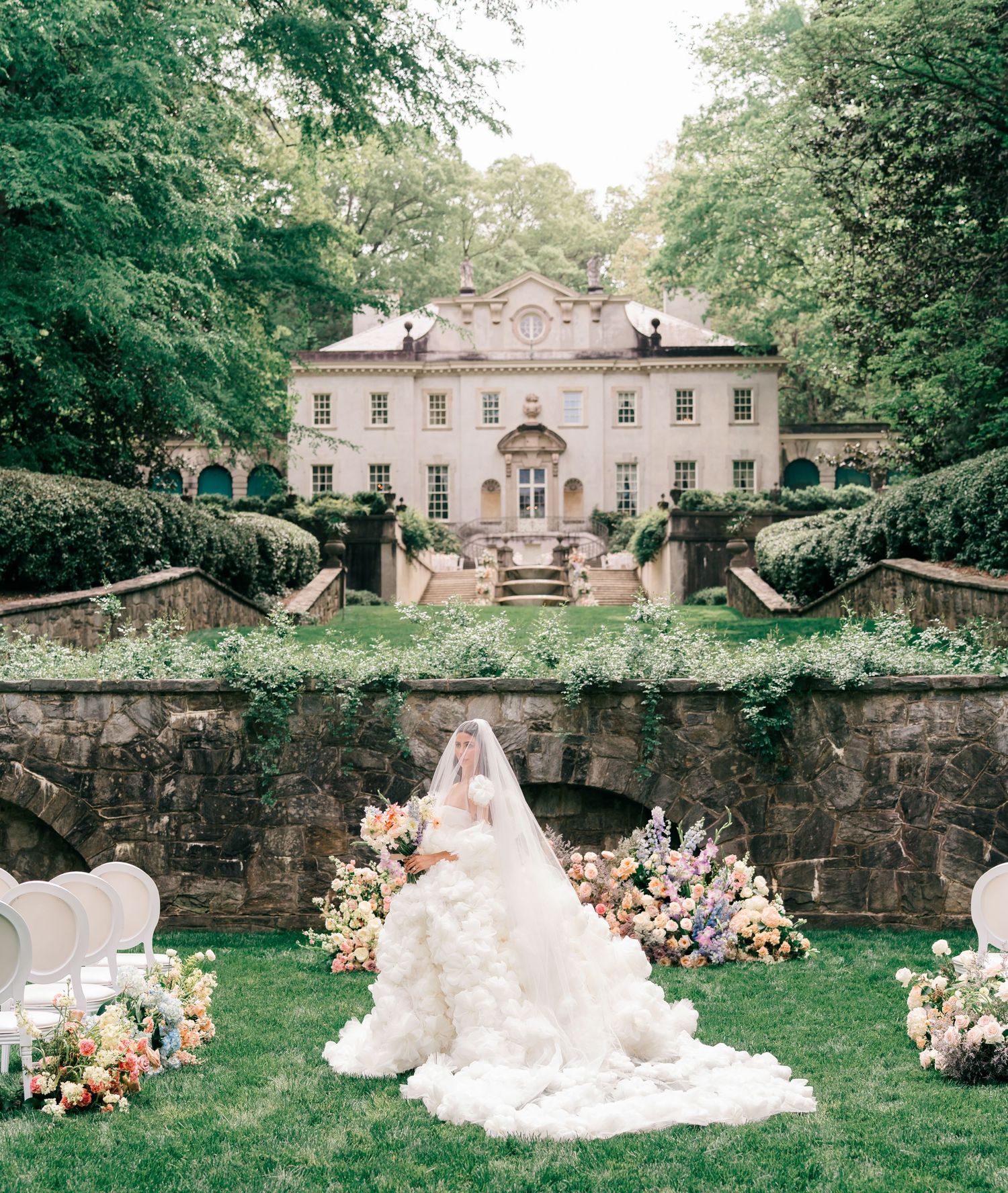 Bride in voluminous white gown seated before floral arrangements at elegant Swan House mansion wedding ceremony.