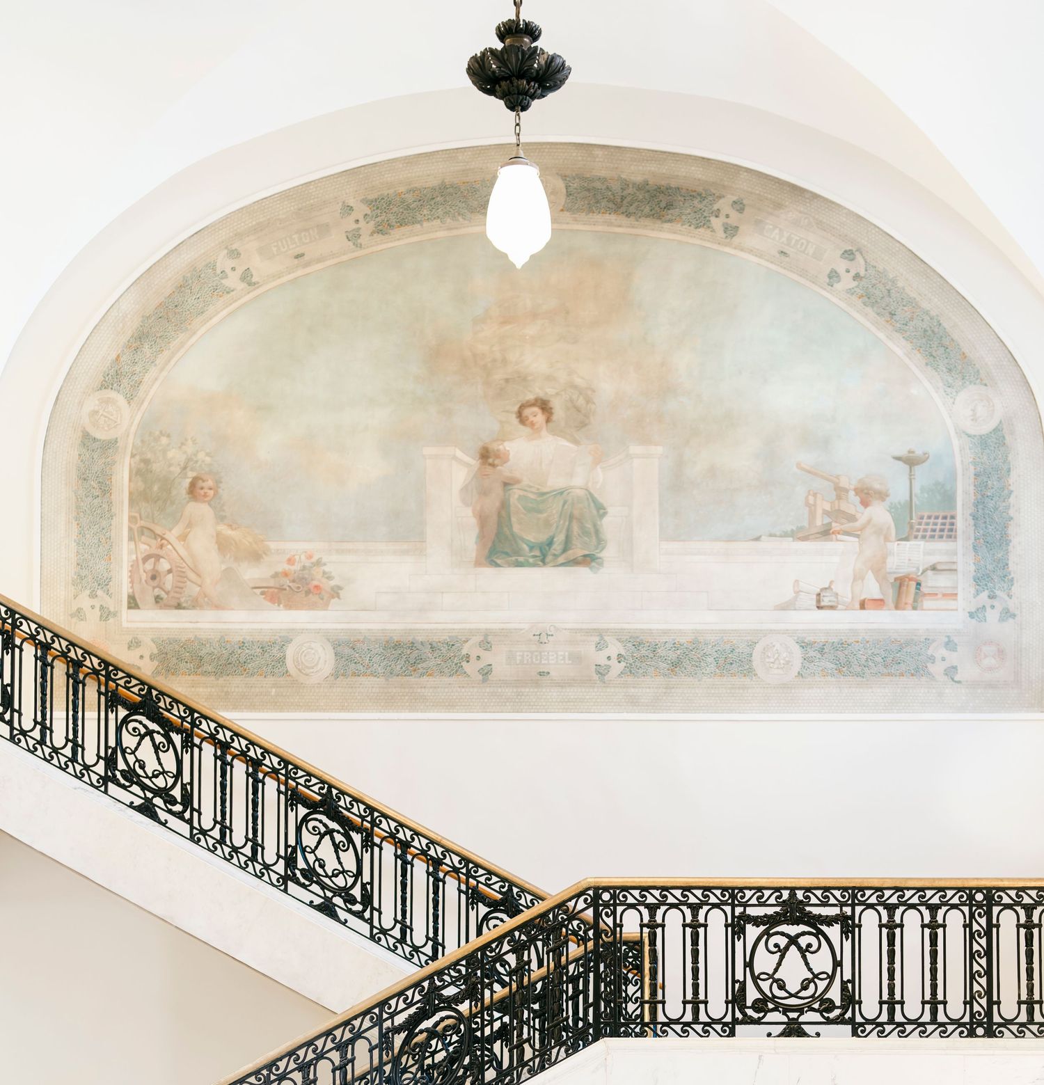 Elegant white arched hallway with ornate wrought iron railings and delicate ceiling frescoes in a historic building.
