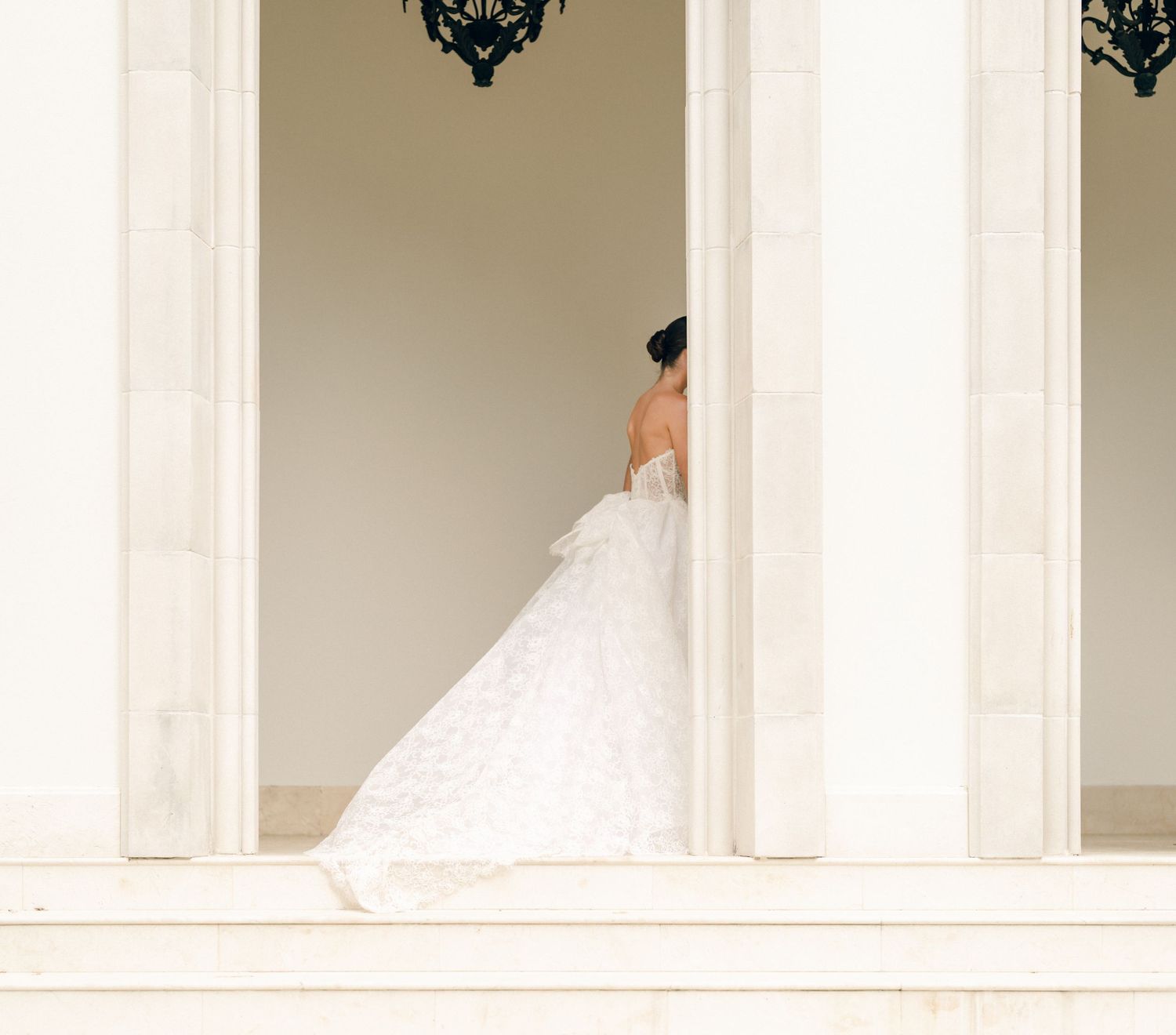 Ethereal white corridor with flowing wedding dress silhouettes visible through arched doorways.