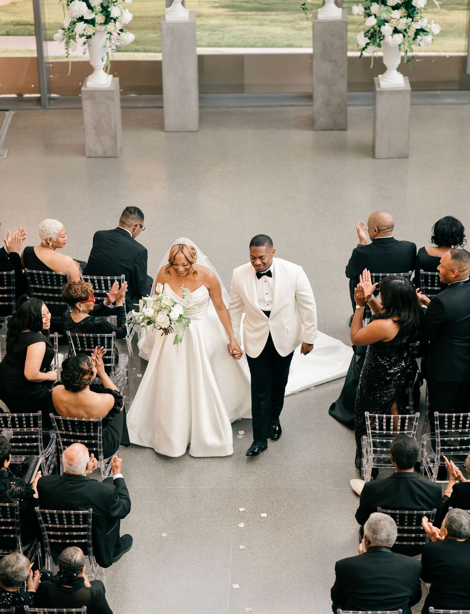Wedding ceremony in a modern venue with elegant white floral arrangements on tall pedestals decorating the aisle.