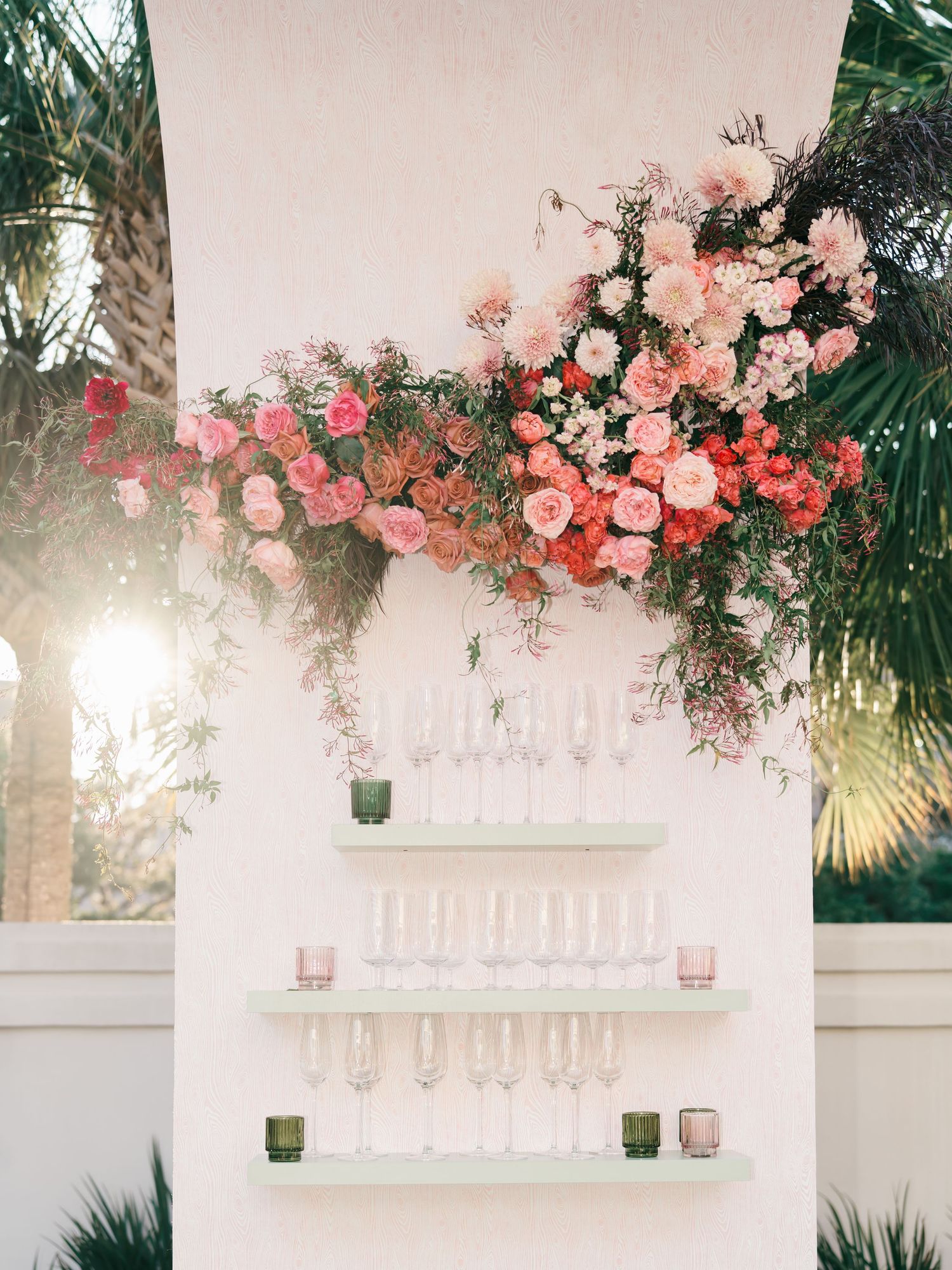 Romantic pink and coral floral arrangements adorn a white pergola in a lush outdoor garden setting.